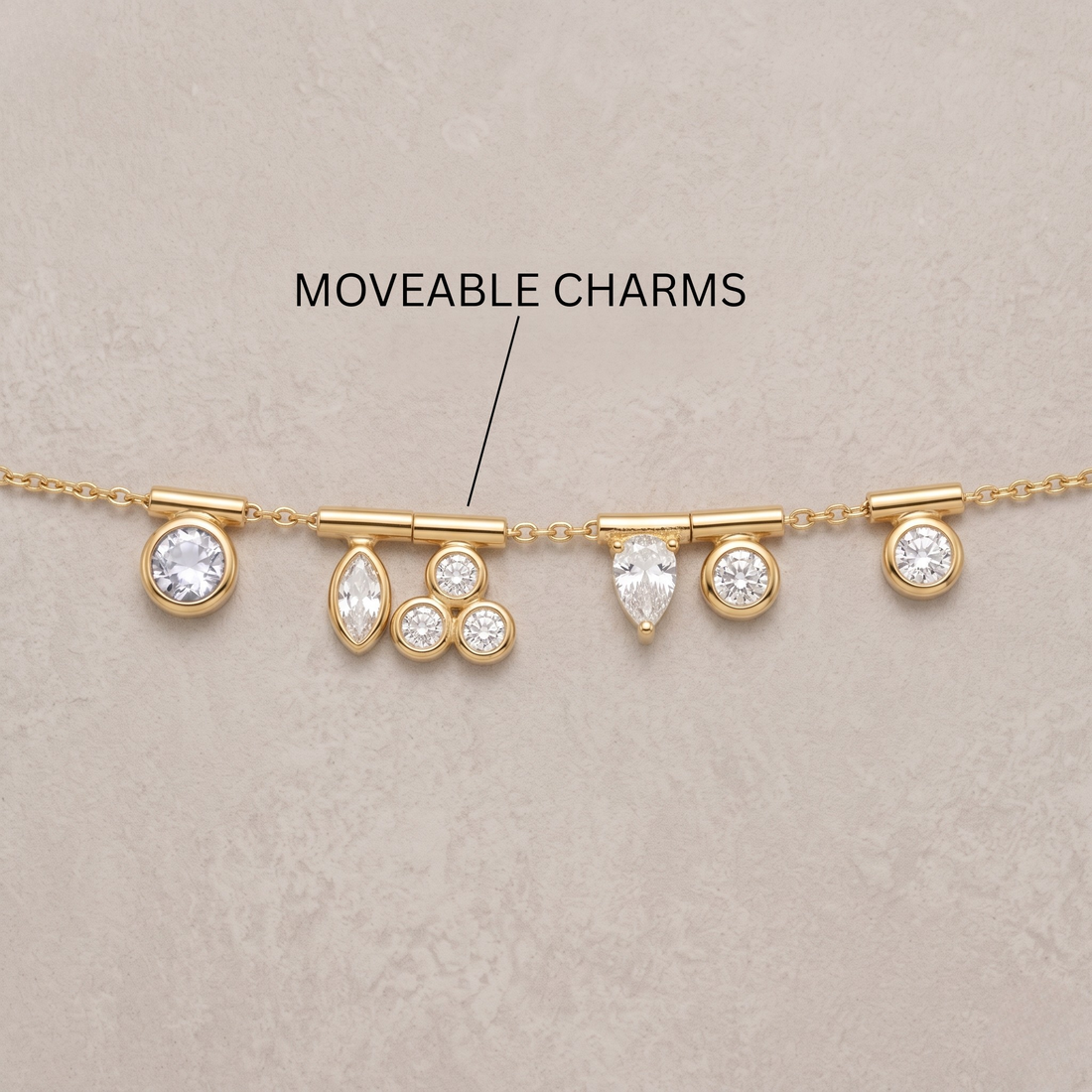 A gold chain necklace with multiple dangling clear gemstone charms, shown on a light beige textured background with an overlaid label reading 'MOVEABLE CHARMS' and an arrow pointing to the center section.