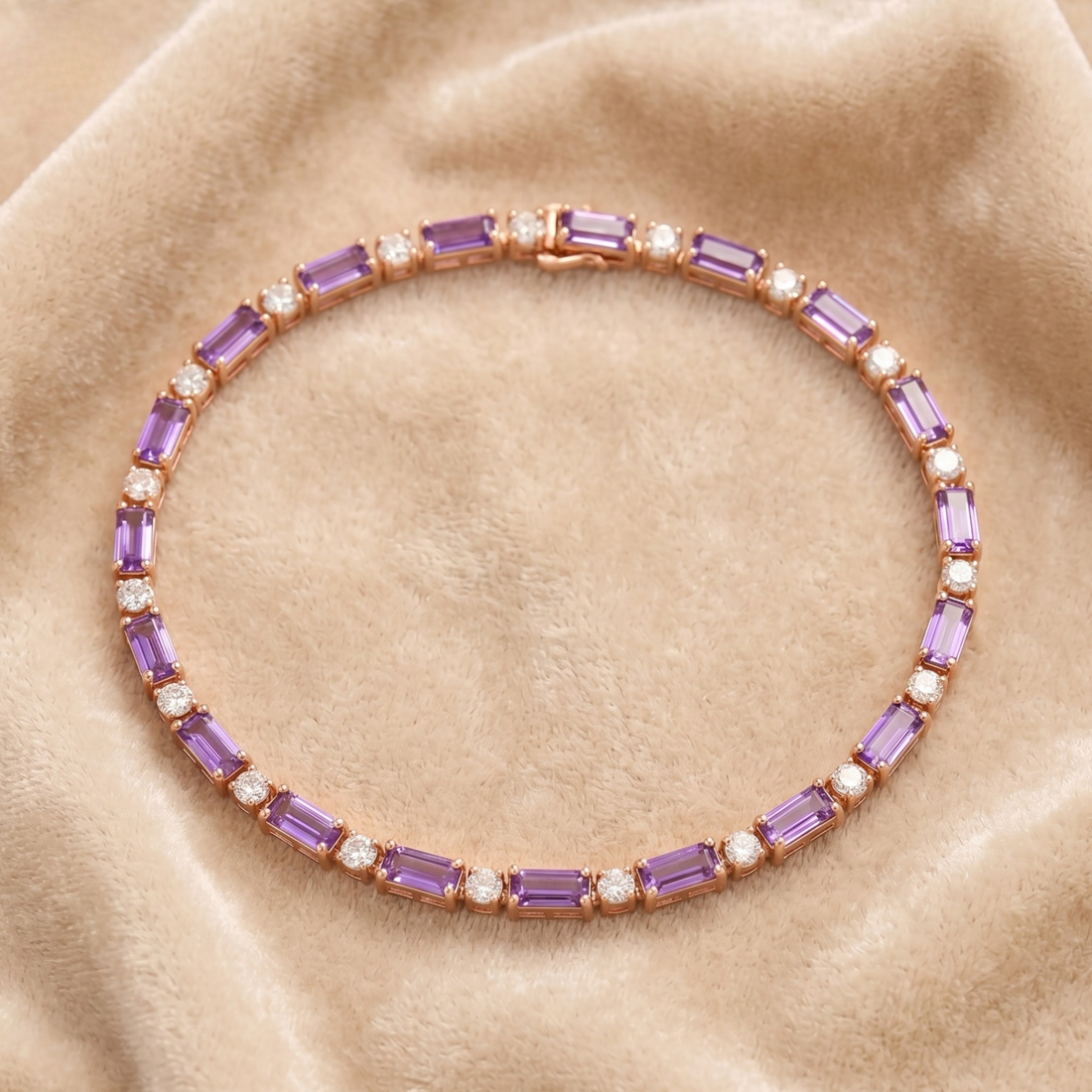 A rose gold tennis bracelet featuring baguette purple amethyst and round white cubic zirconia stones, displayed on a beige velvet fabric background.