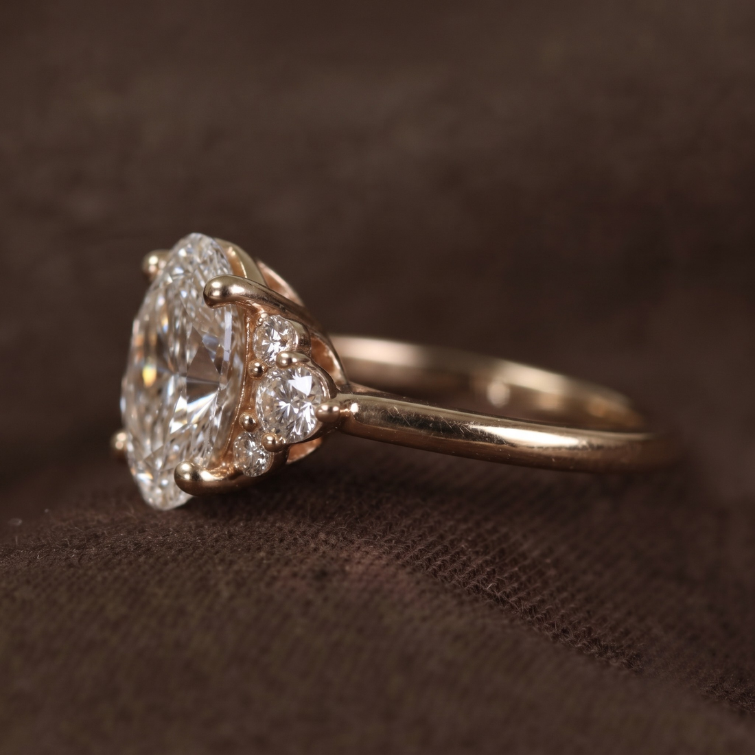 A close-up shot of a vintage diamond ring with a large round-cut center stone and smaller diamonds on the shoulders, set in a yellow gold band, resting on a textured dark brown surface.