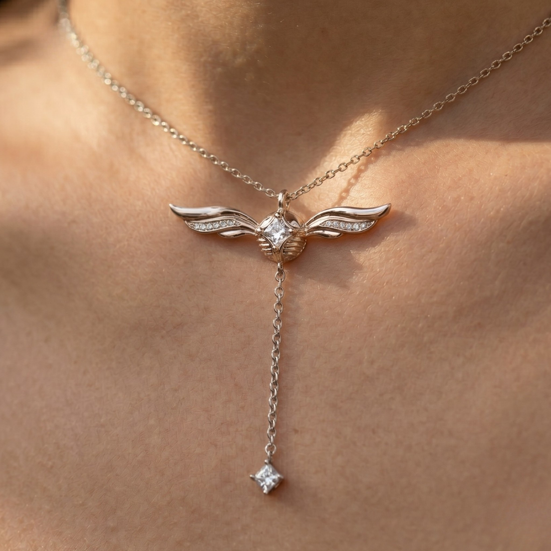A close-up of a delicate silver-toned wing pendant necklace worn on a person's neck. The wing pendant has small clear stones set along the edges and hangs from a chain with a dangling star-shaped clear gemstone at the end.