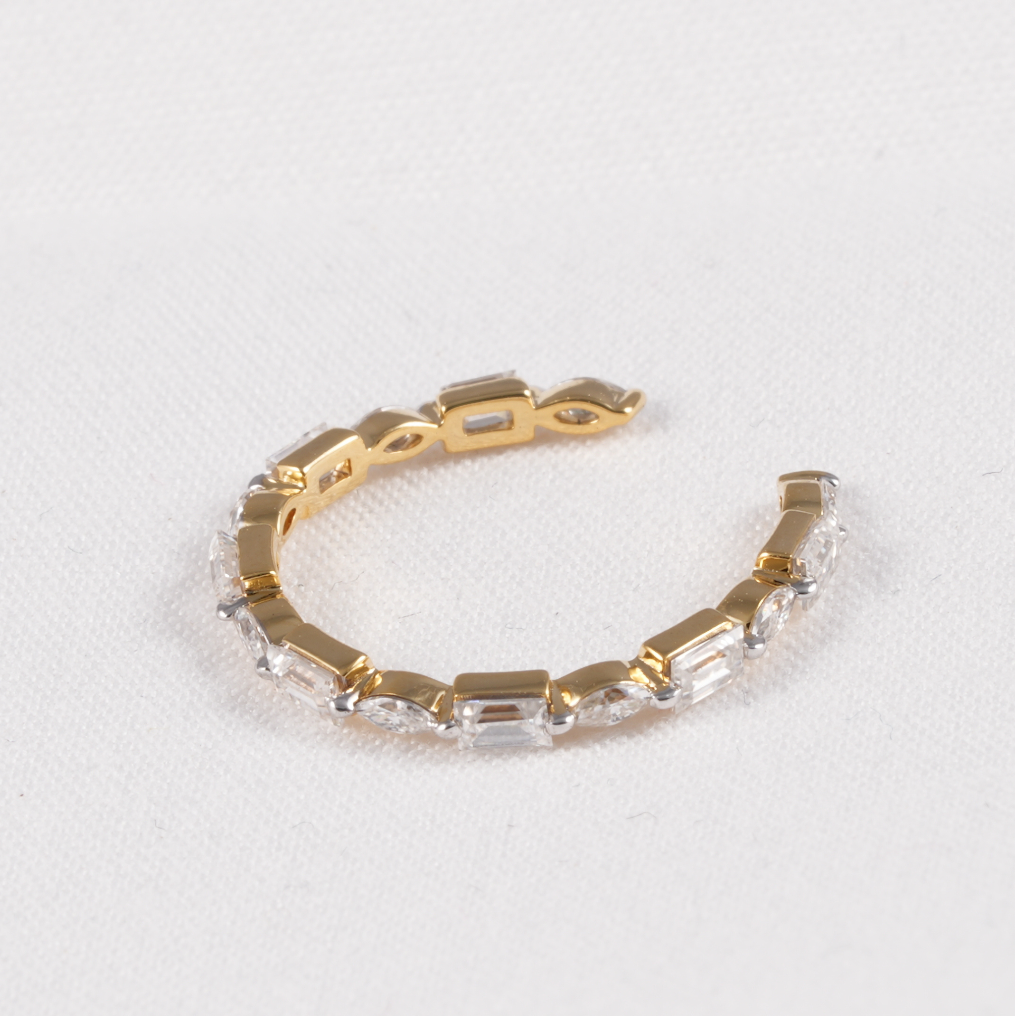 A gold-toned open cuff bracelet featuring clear rectangular baguette-cut gemstones set along the front, displayed on a textured white background.