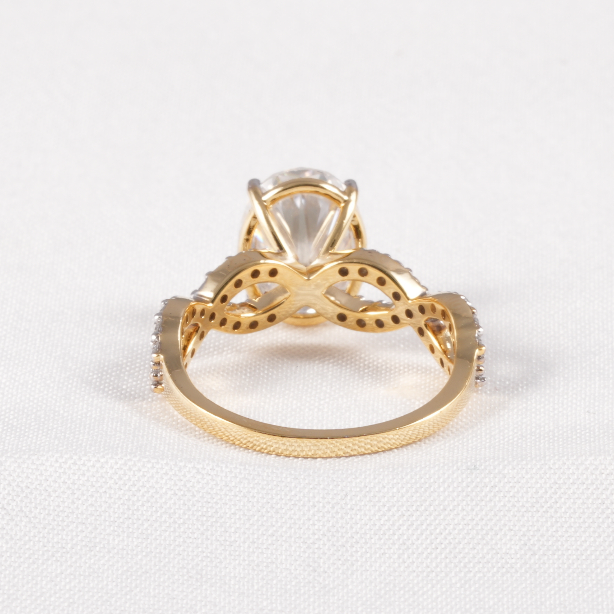 A gold ring with a large clear marquise-cut center stone and decorative openwork detailing on the shoulders, photographed on a white textured fabric background.