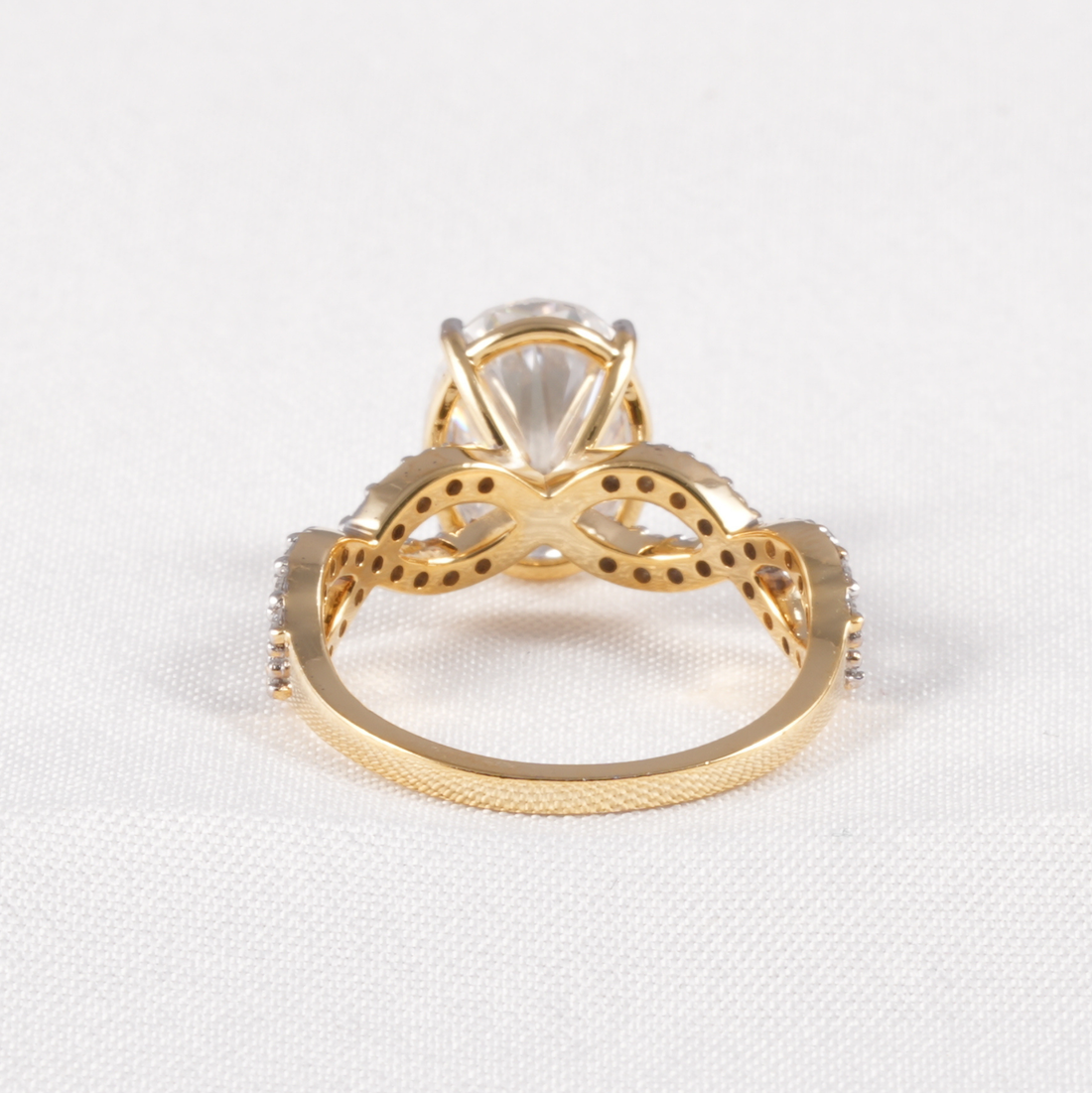 A gold ring with a large clear marquise-cut center stone and decorative openwork detailing on the shoulders, photographed on a white textured fabric background.