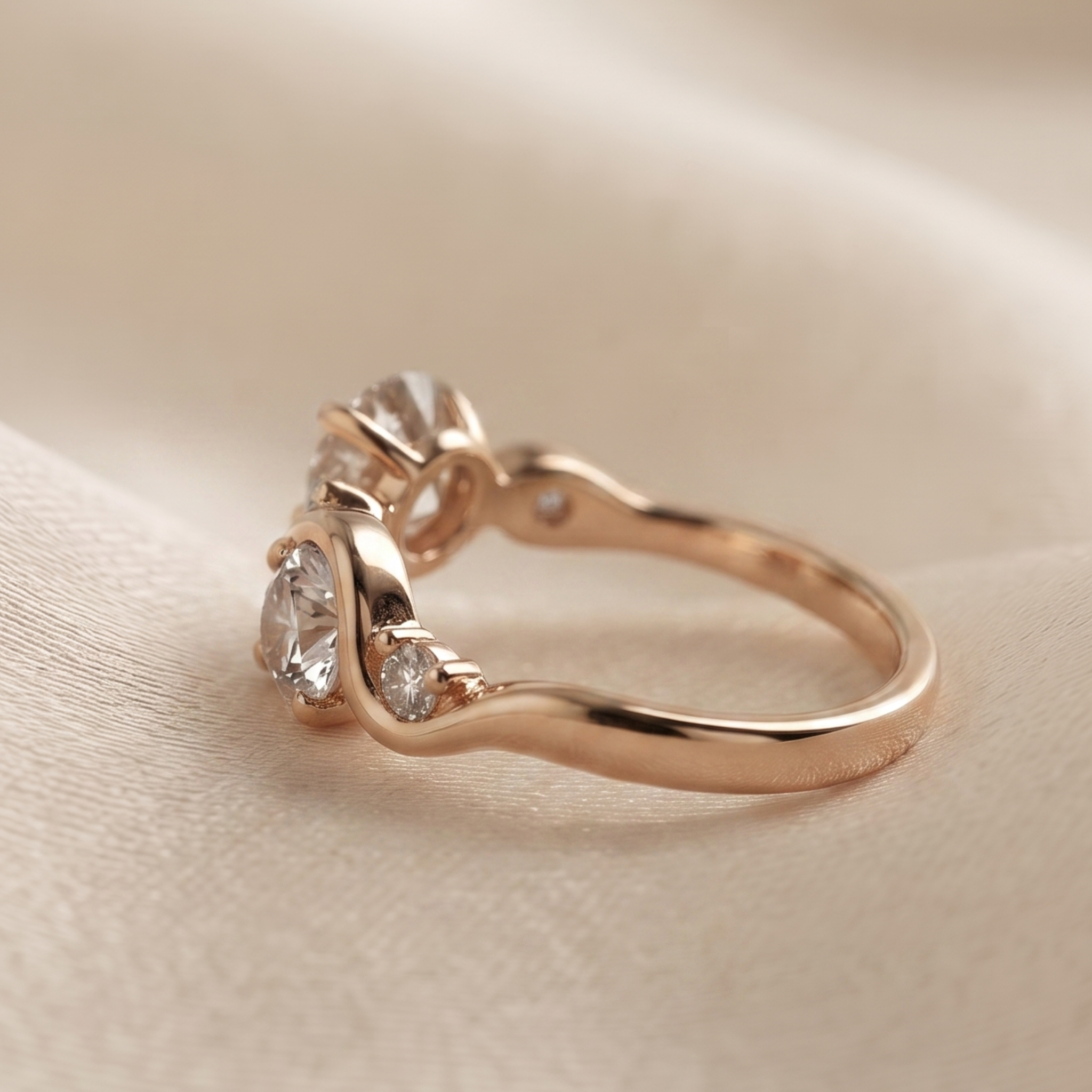 A rose gold three-stone ring with clear gemstones, resting on a soft beige fabric background.