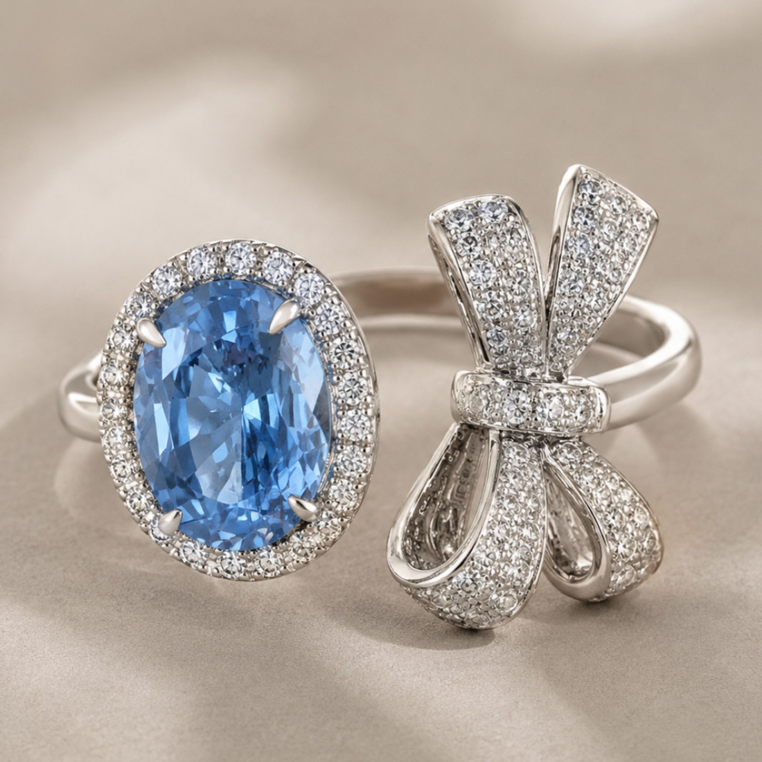 Two silver rings displayed on a soft beige satin background: one ring features a large oval-cut light blue gemstone surrounded by a halo of small clear stones, and the other is a bow-shaped ring paved with clear stones.