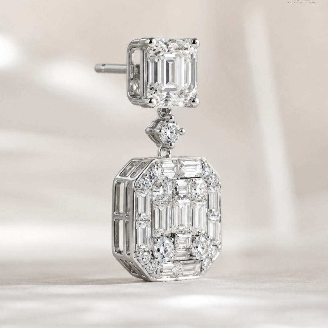 A silver-toned drop earring featuring a square emerald-cut diamond at the top and a larger rectangular baguette and round-cut diamond pavé setting below, shown on a soft light beige background.