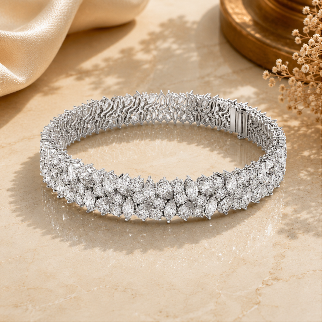 A sparkling diamond tennis bracelet in a silver-toned setting, displayed on a beige marble surface with elegant fabric and dried flowers in the background.