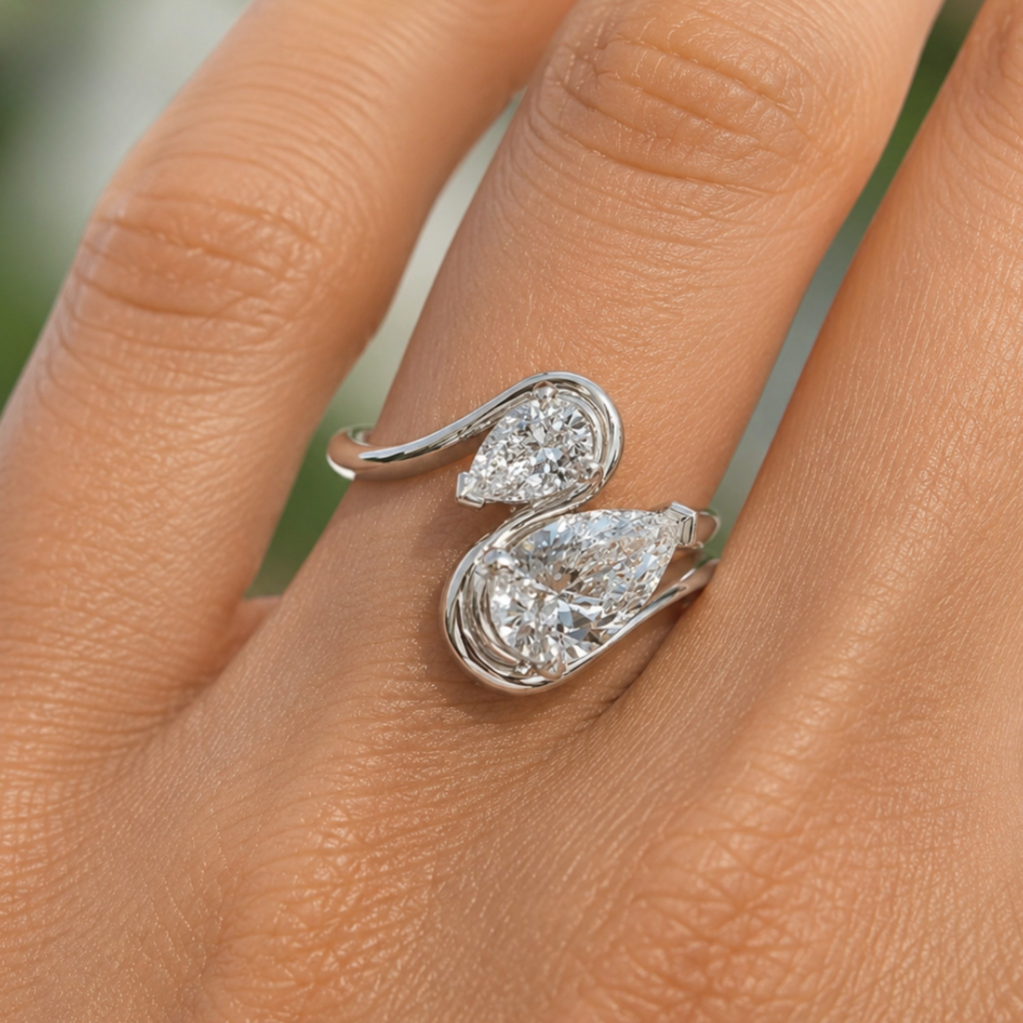 A close-up of a silver ring with two pear-cut clear gemstones on a person's finger.