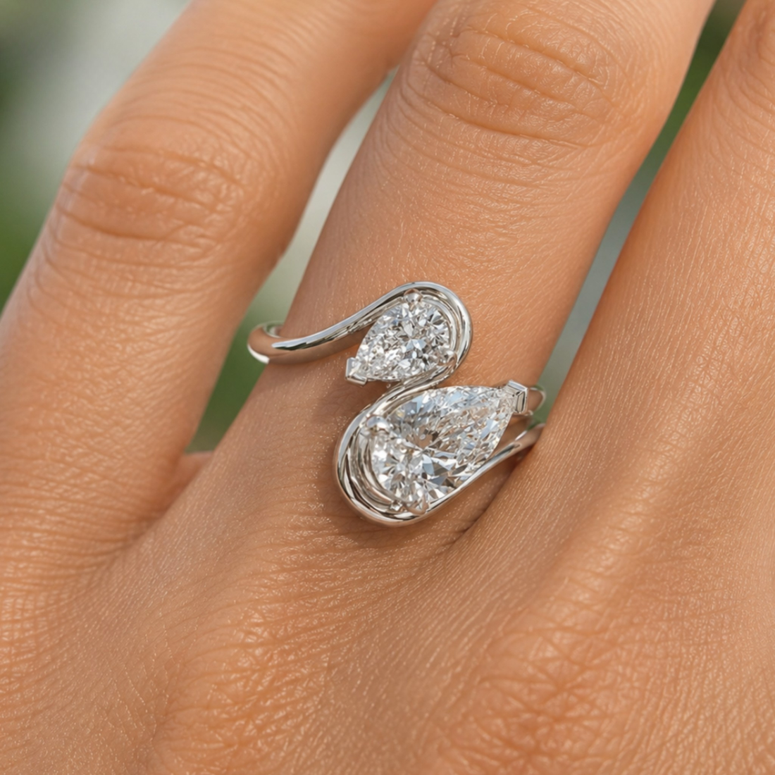 A close-up of a silver ring with two pear-cut clear gemstones on a person's finger.