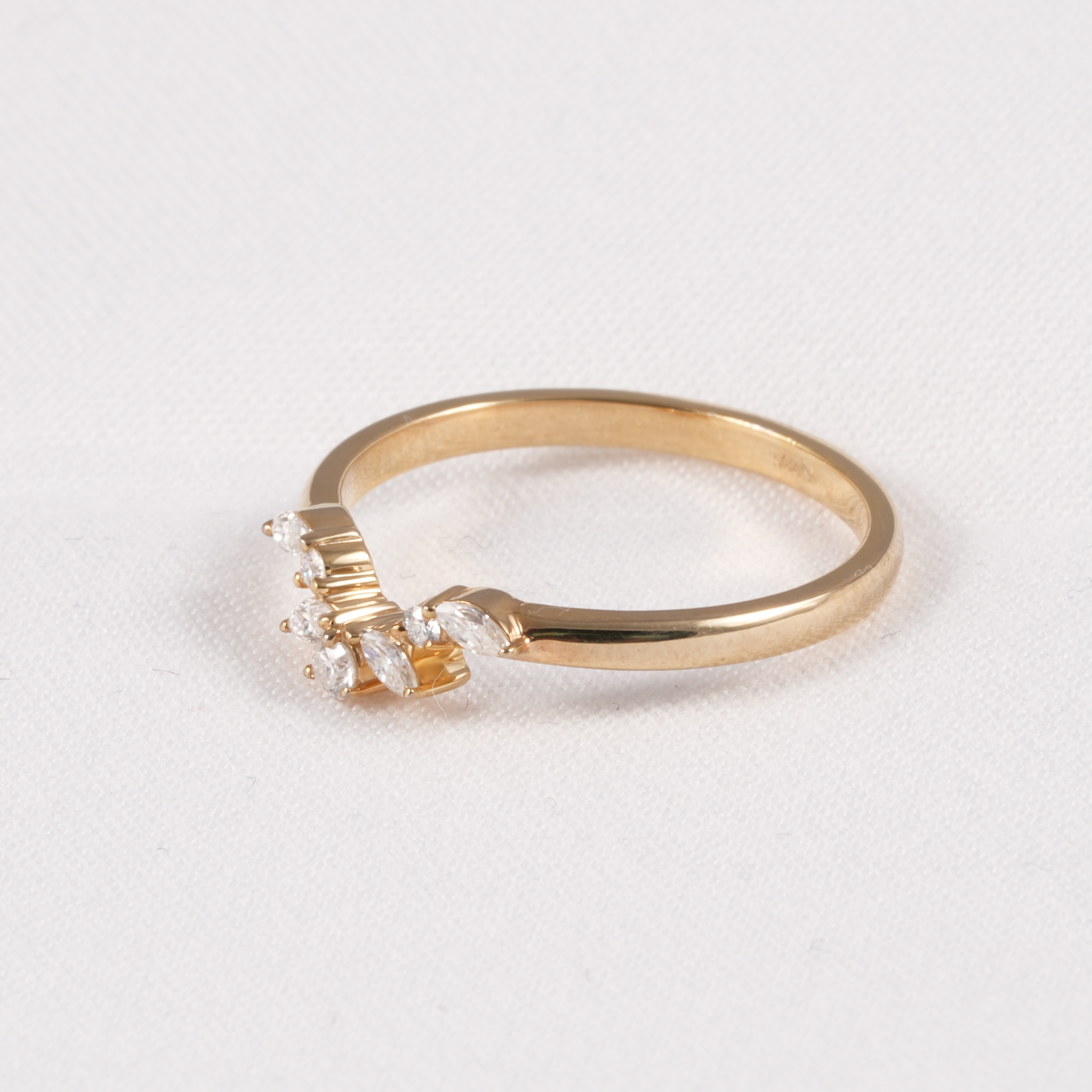 A gold ring with a small cluster of clear gemstones on the front, photographed on a plain light background.