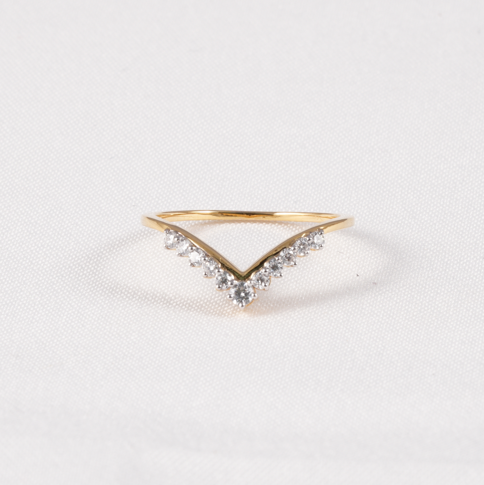 A gold V-shaped ring with small clear stones along the top, photographed on a light textured white background.