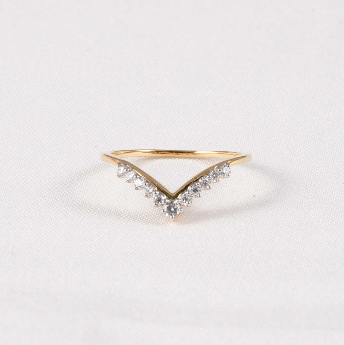 A gold V-shaped ring with small clear stones along the top, photographed on a light textured white background.