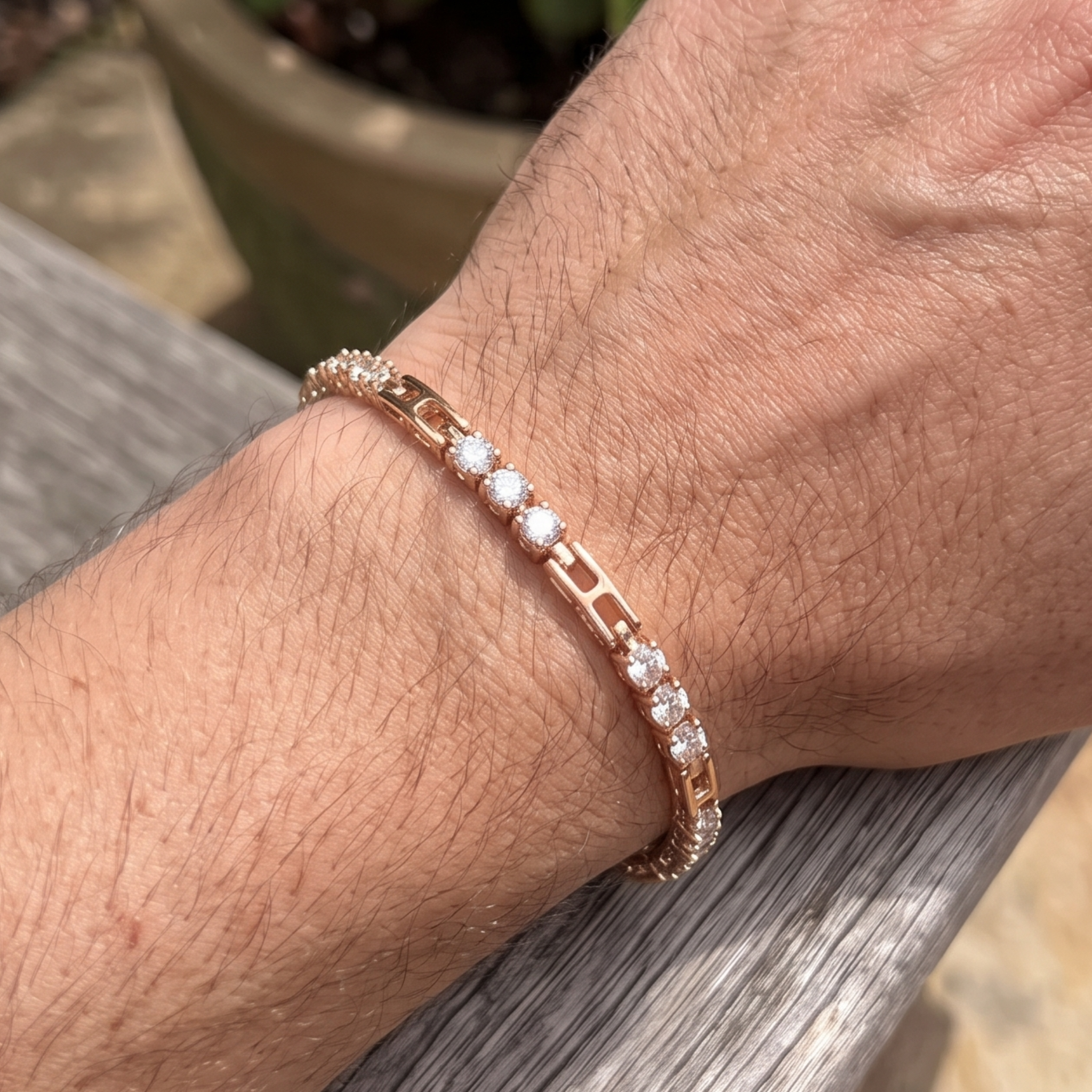 A rose gold tennis bracelet with clear round-cut gemstones worn on a person's wrist, resting on a weathered gray wooden surface.