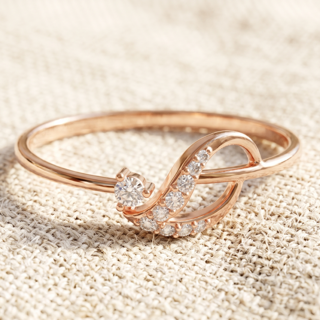 A rose gold ring with a curved infinity-style design, featuring a single round-cut diamond and a pavé band of small clear stones, resting on a textured beige linen background.