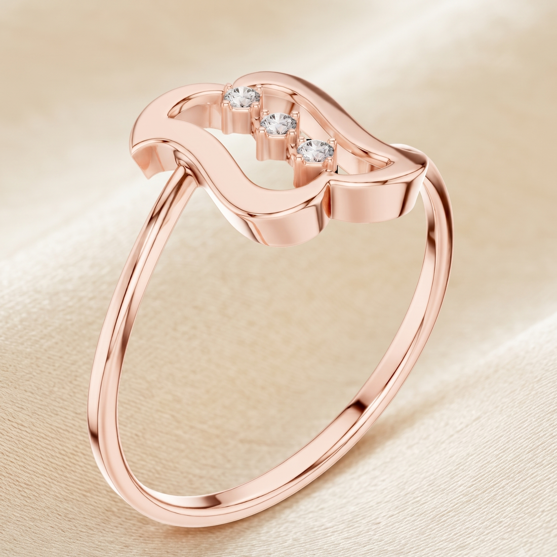 A rose gold open-band ring with a wavy top setting and three small clear stones, photographed on a soft beige fabric background.