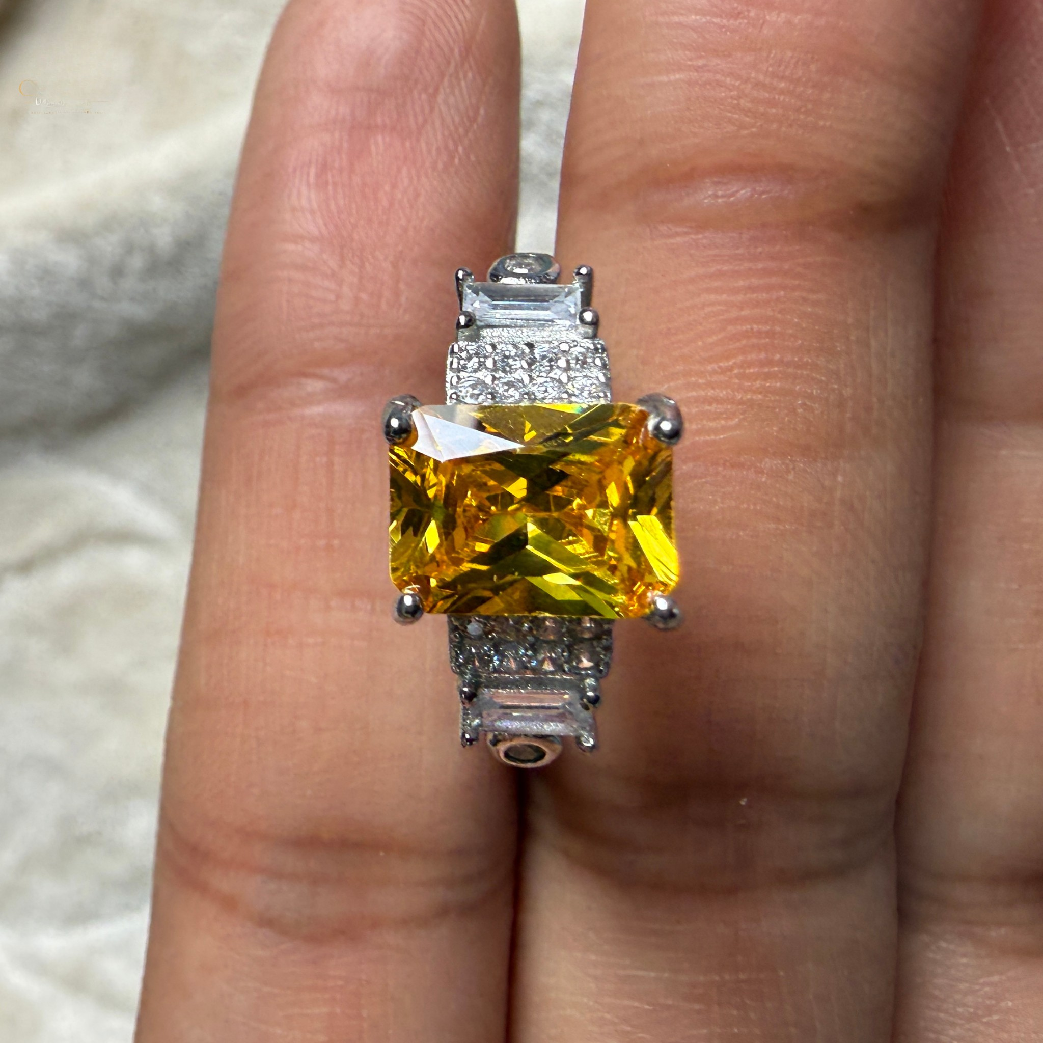 A yellow cushion-cut diamond ring with a silver-toned setting, shown worn on a person's finger.