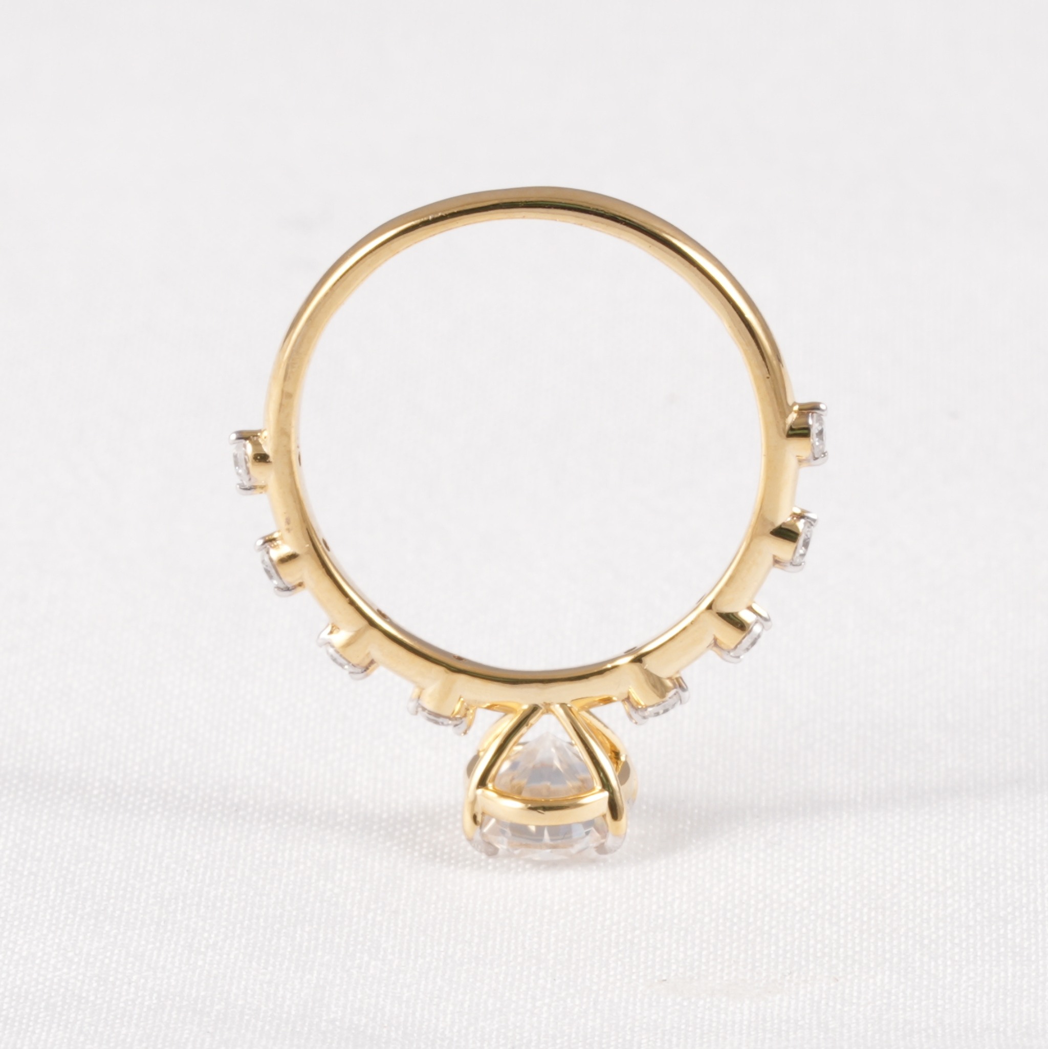 A gold ring with a large clear triangular center stone and smaller clear stones along the band, photographed on a white textured background.