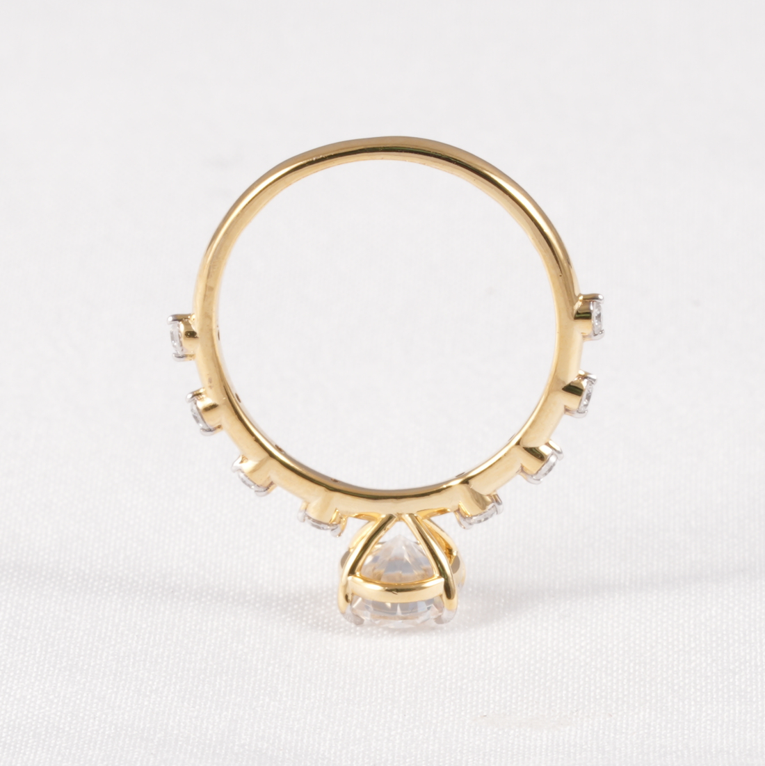 A gold ring with a large clear triangular center stone and smaller clear stones along the band, photographed on a white textured background.