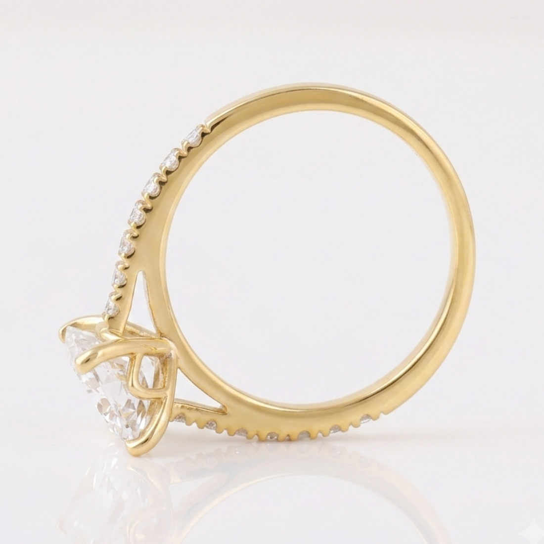 A yellow gold ring featuring a large clear round-cut center stone and a pavé-set row of small clear stones along the shank, shown on a white reflective surface.