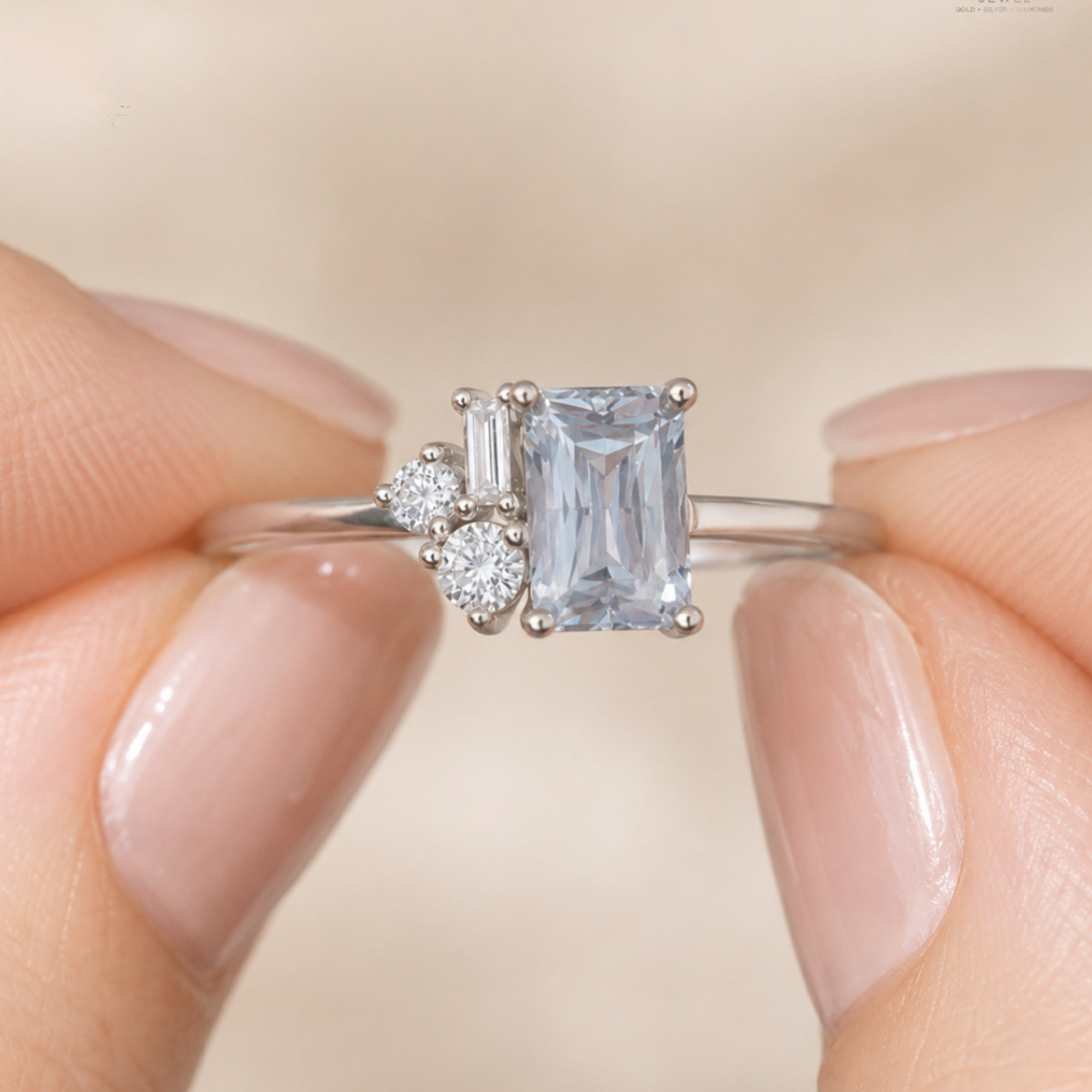 A close-up of a silver ring with a large emerald-cut light blue center stone and two small clear accent stones, held between fingers against a soft beige background.