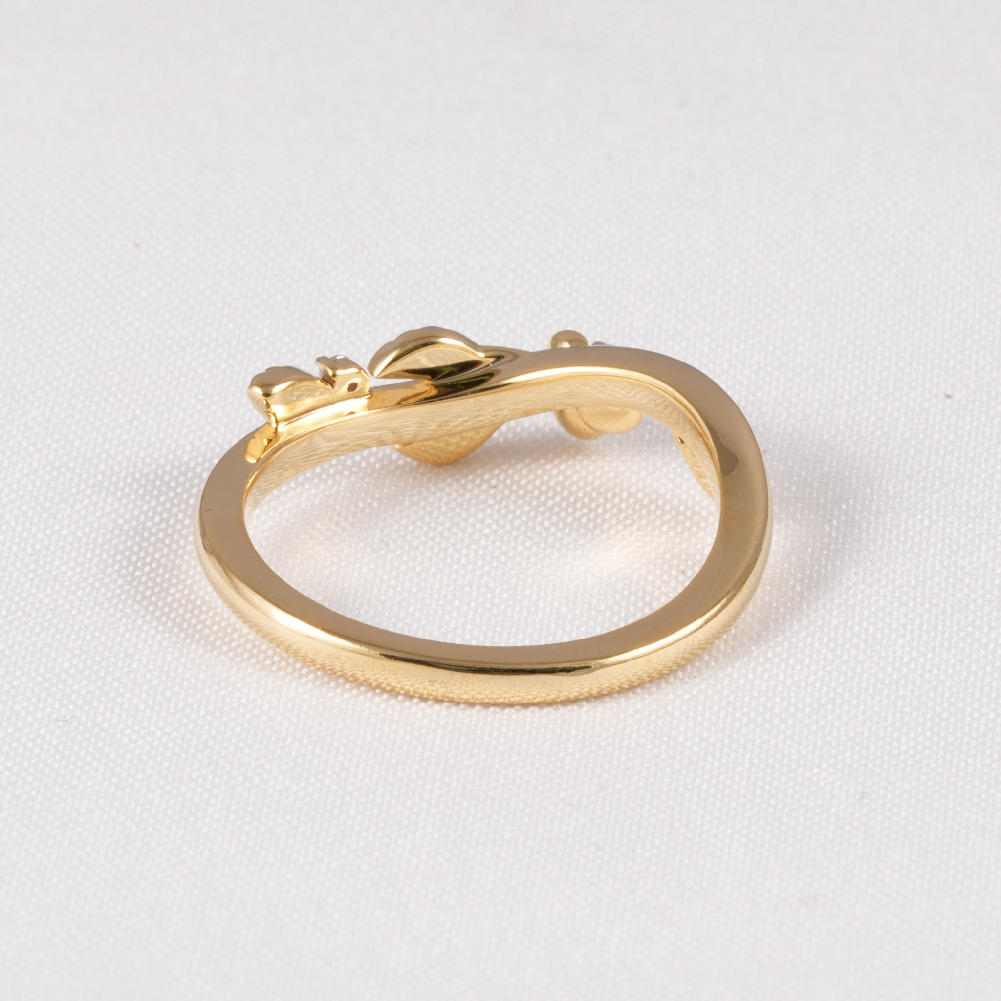 A polished gold ring with a unique curved, snake-like or snake-head design, displayed on a textured white fabric background.