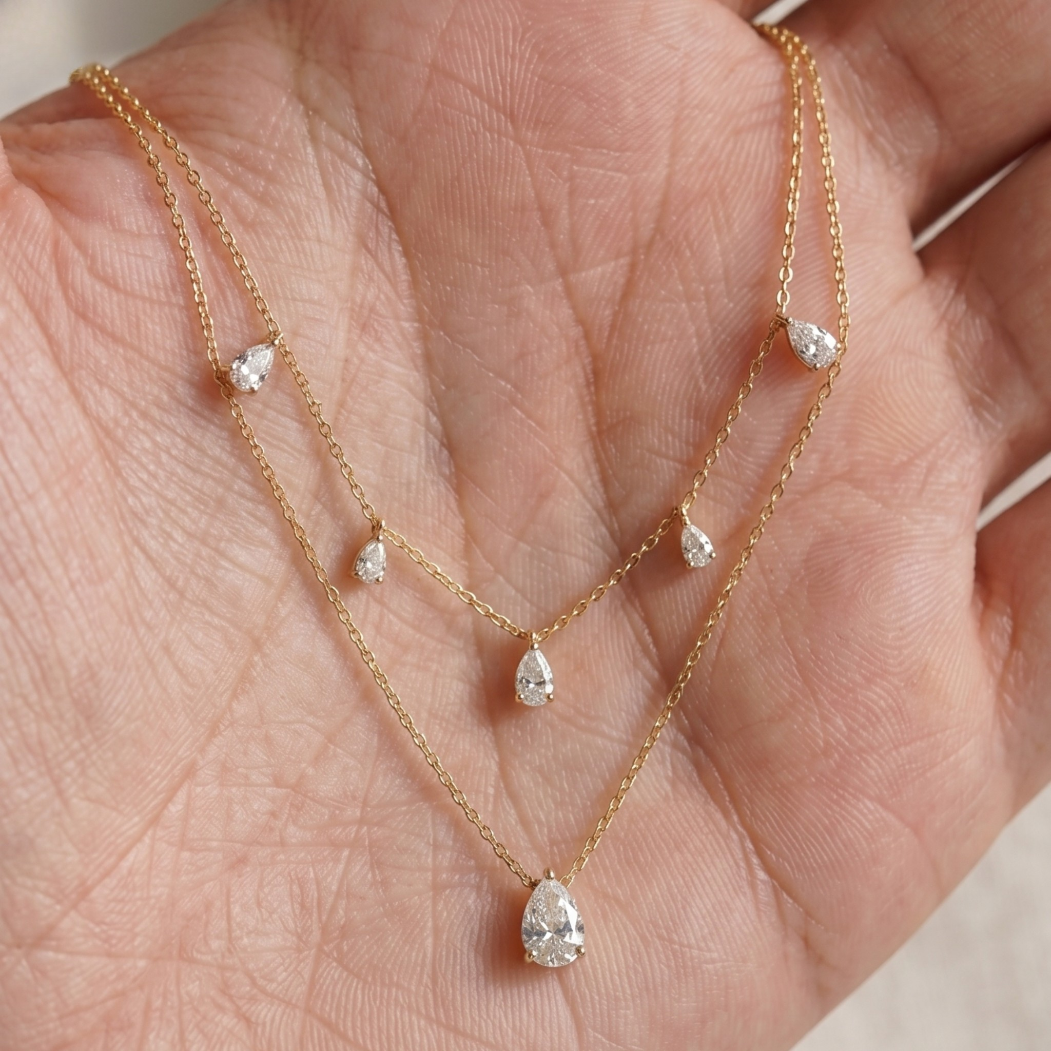 A delicate double-layered gold necklace with small teardrop-shaped clear gemstones, displayed on a person's palm.