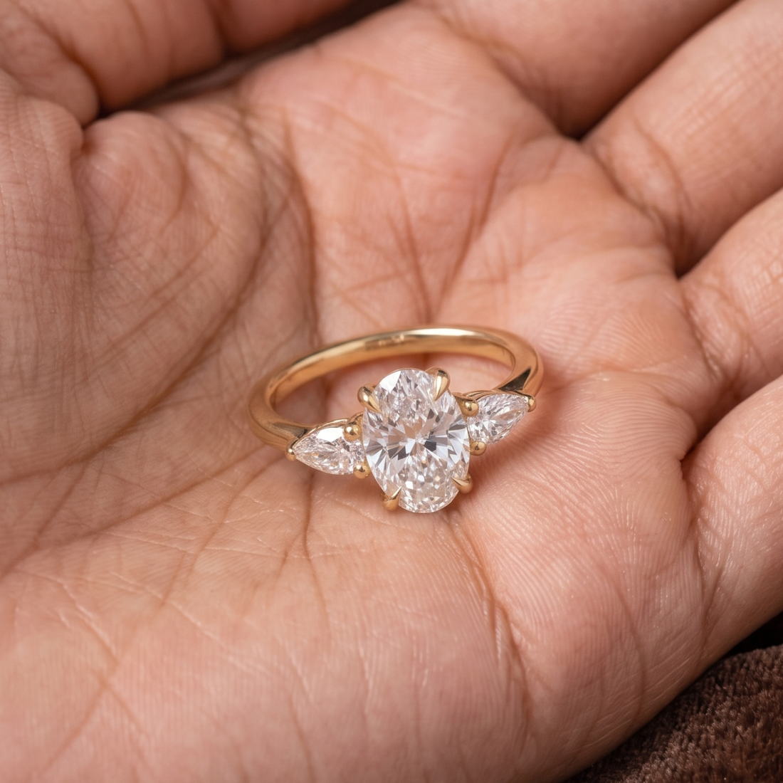 A gold ring with a clear oval center stone and marquise-cut side stones, resting on an open hand.