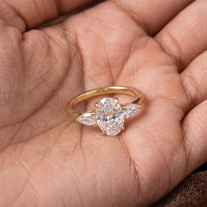 A gold ring with a clear oval center stone and marquise-cut side stones, resting on an open hand.