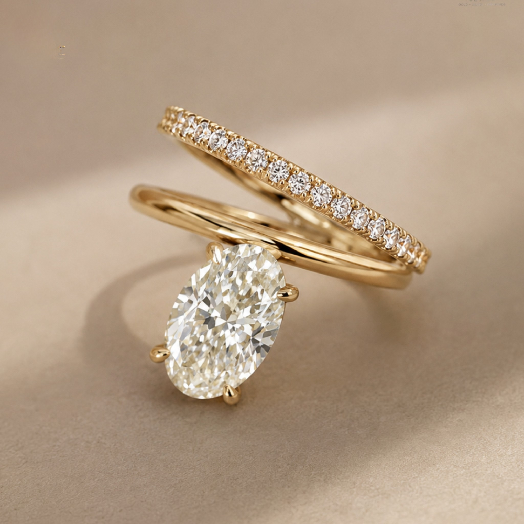 A gold engagement ring with a large oval-cut clear center stone and a matching gold wedding band featuring a row of small clear stones, photographed on a soft beige background.
