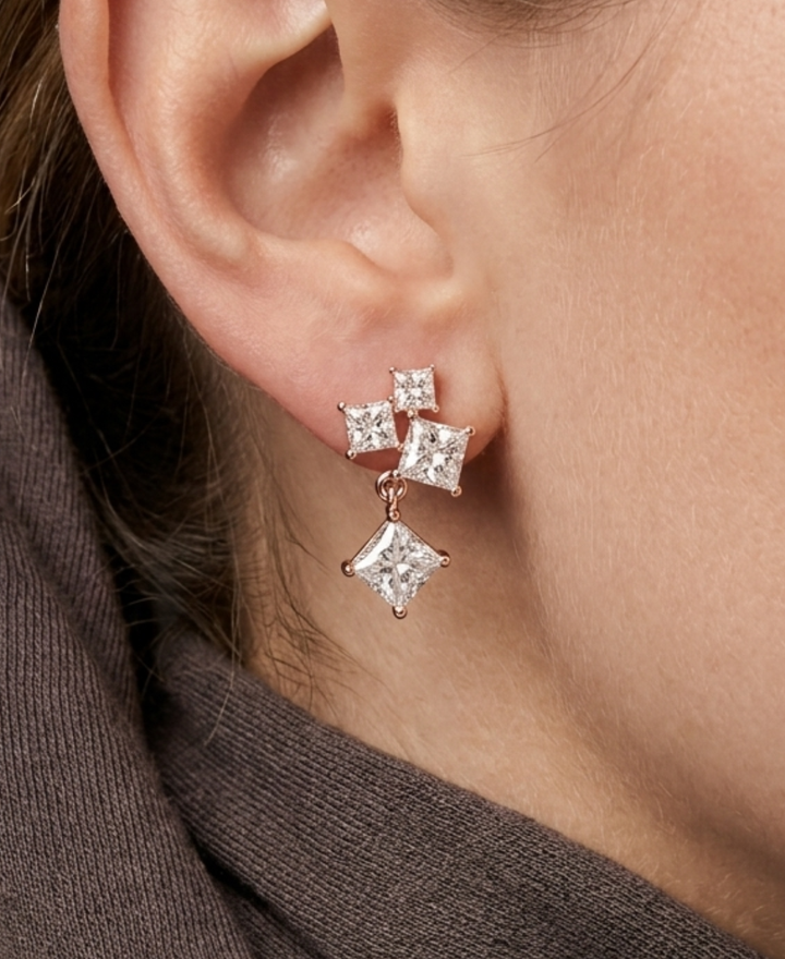 Rose gold princess-cut diamond earrings displayed on neutral fabric under soft natural light.