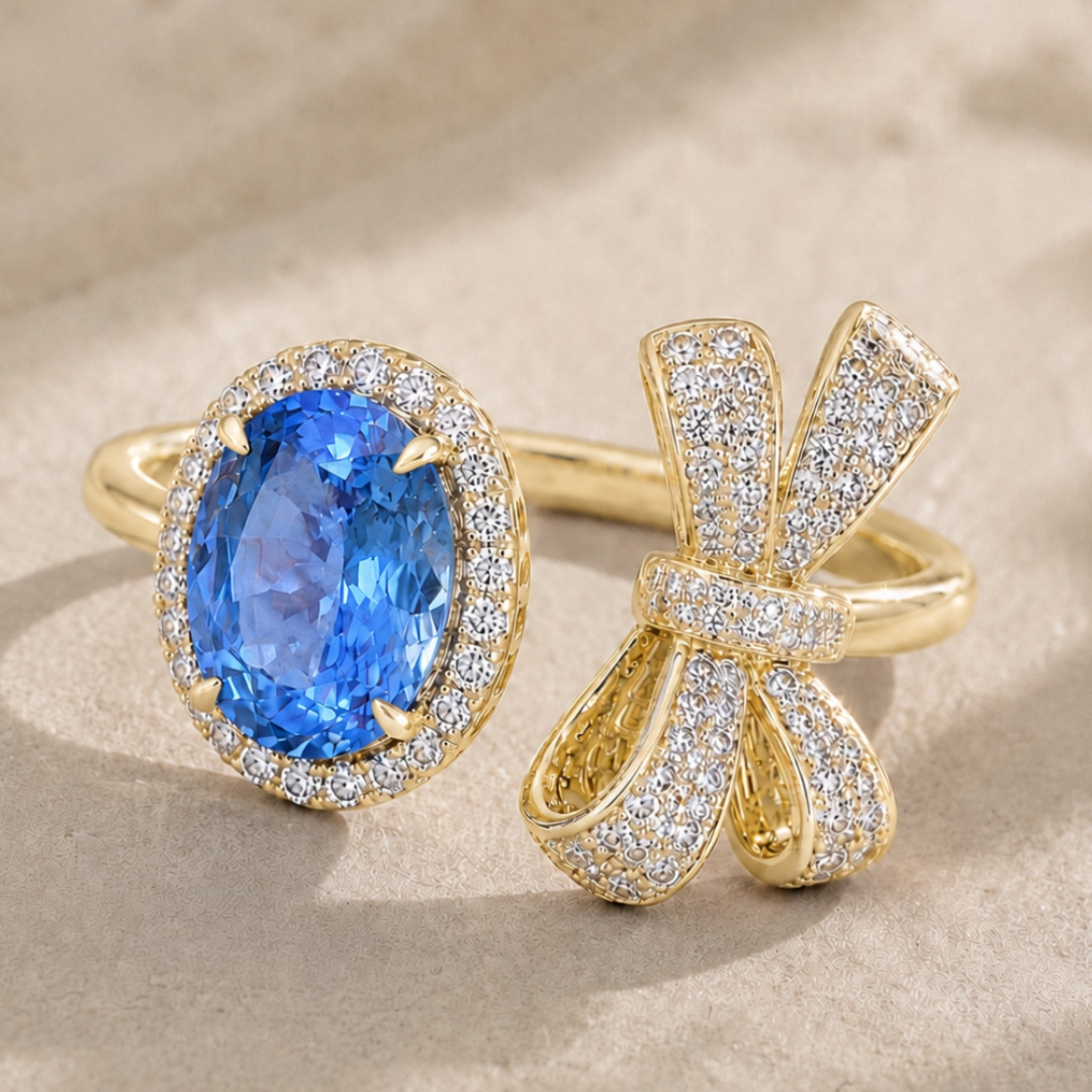 Two gold rings displayed on a beige textured surface: one with an oval blue gemstone surrounded by small clear stones, and the other shaped like a bow, paved with clear stones.