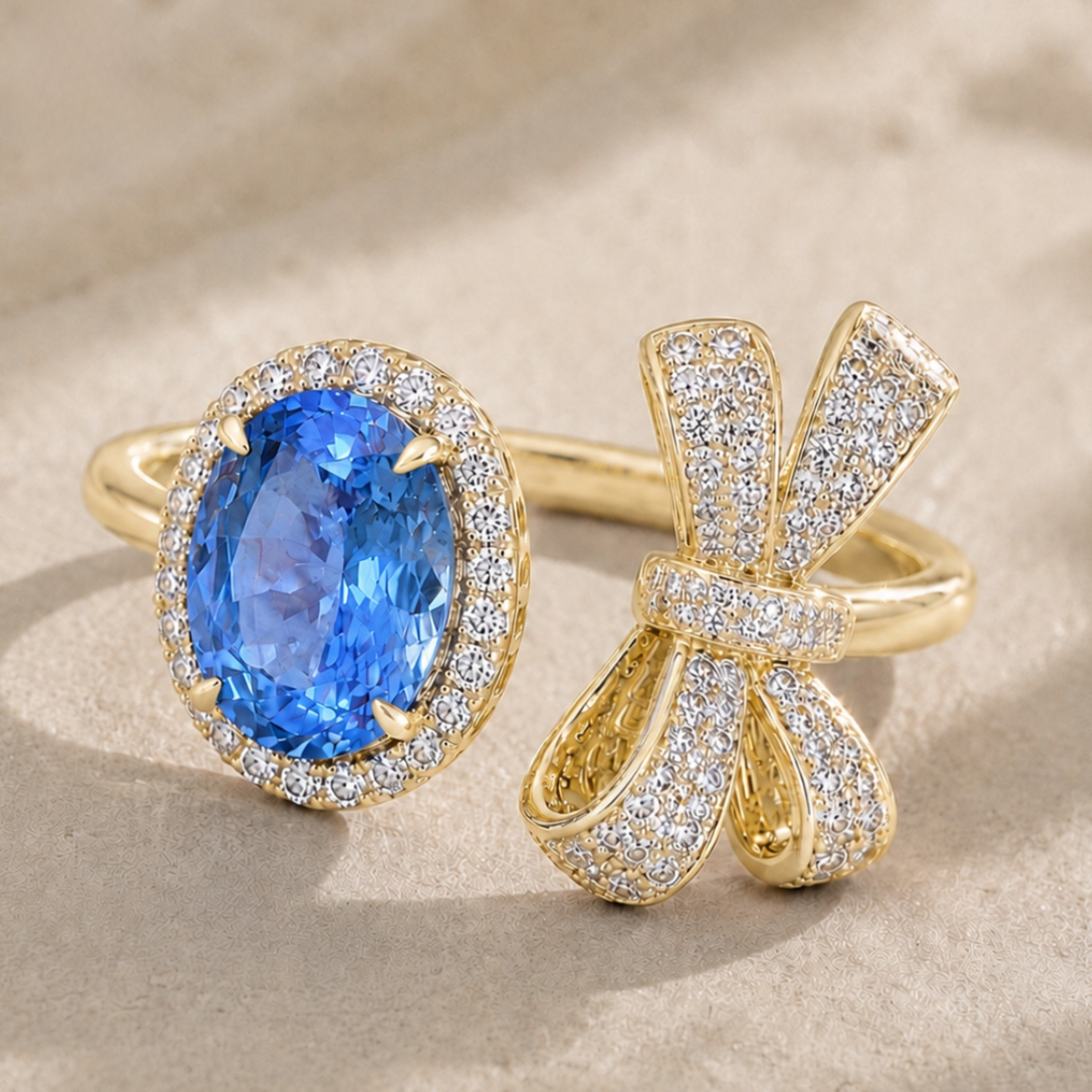 Two gold rings displayed on a beige textured surface: one with an oval blue gemstone surrounded by small clear stones, and the other shaped like a bow, paved with clear stones.