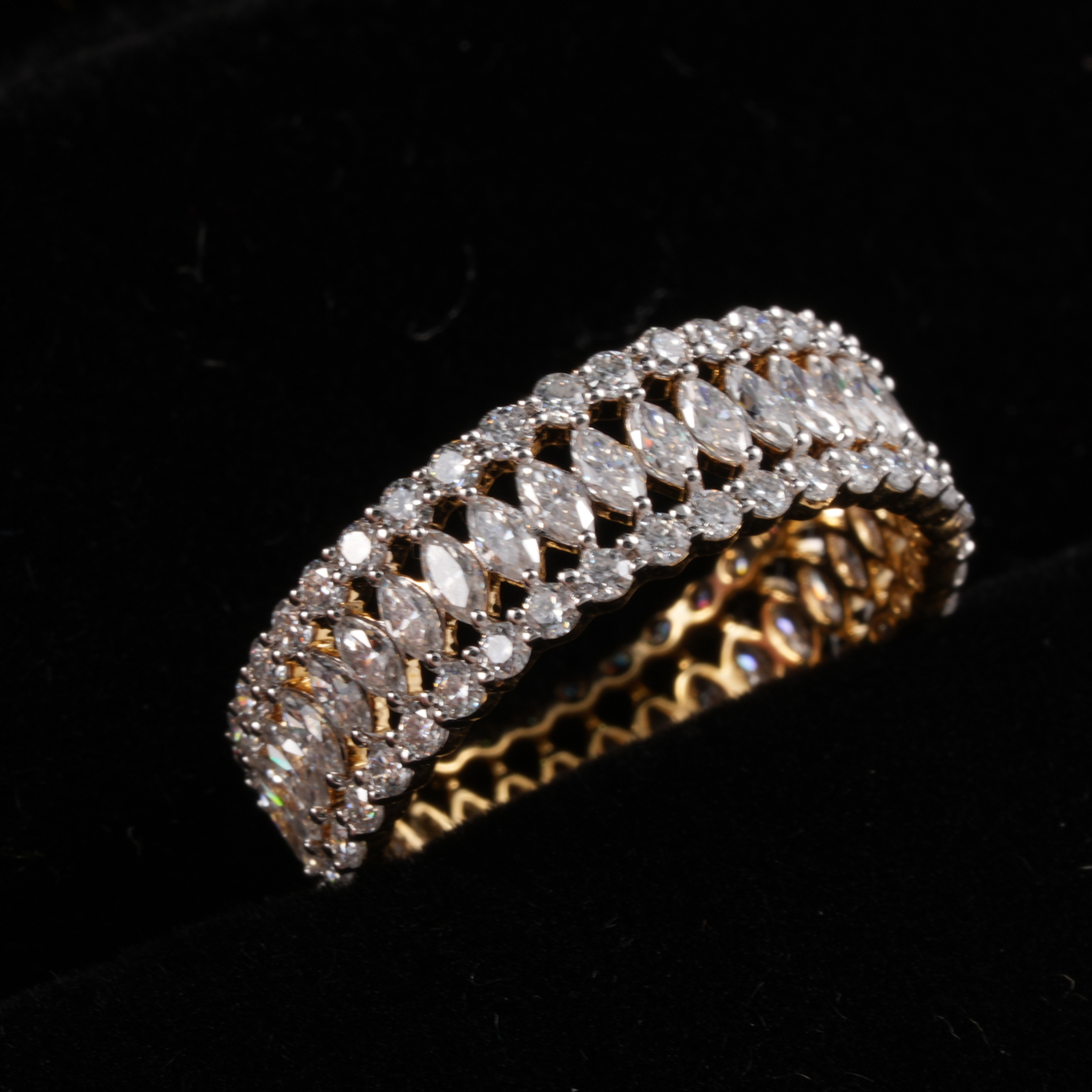 A double-row diamond eternity ring in yellow gold and silver-tone metal, set with marquise-cut and round diamonds on a black velvet background.