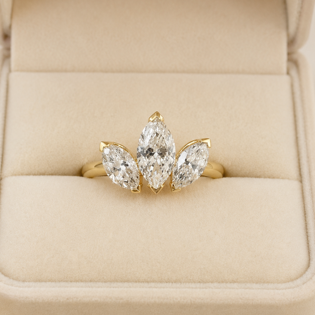A yellow gold ring with three marquise-cut clear gemstones arranged in a fan shape, displayed in a cream-colored ring box.