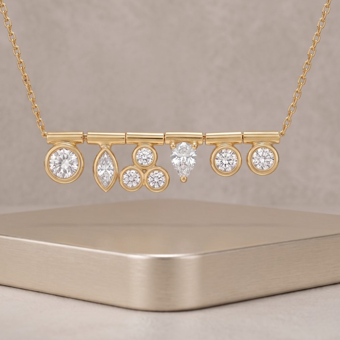 A gold bar necklace with multiple dangling diamond settings, displayed on a neutral beige surface against a matching background.
