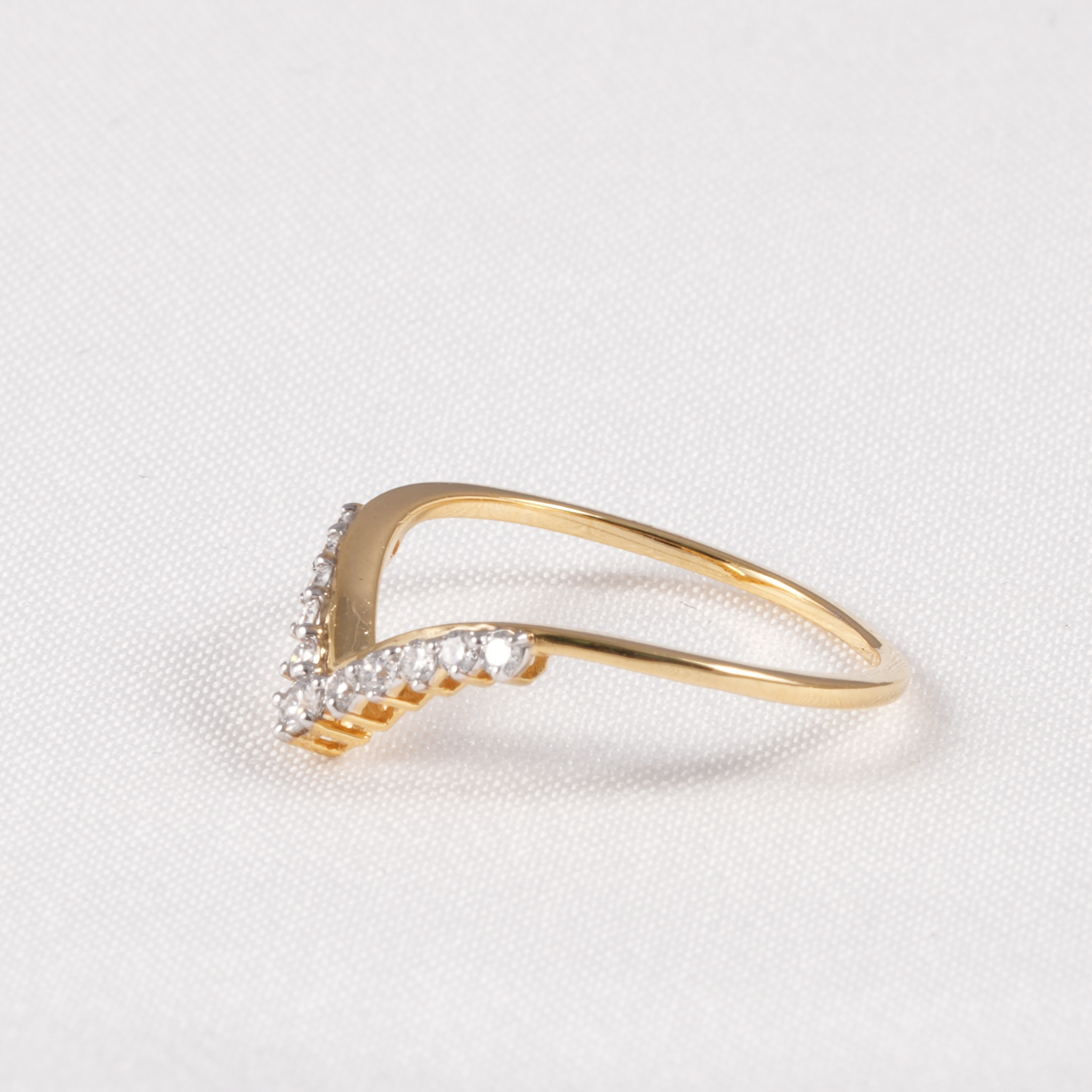 A gold V-shaped ring with small clear pavé stones along the front, photographed on a textured white fabric background.