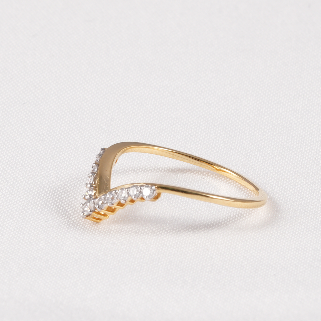 A gold V-shaped ring with small clear pavé stones along the front, photographed on a textured white fabric background.