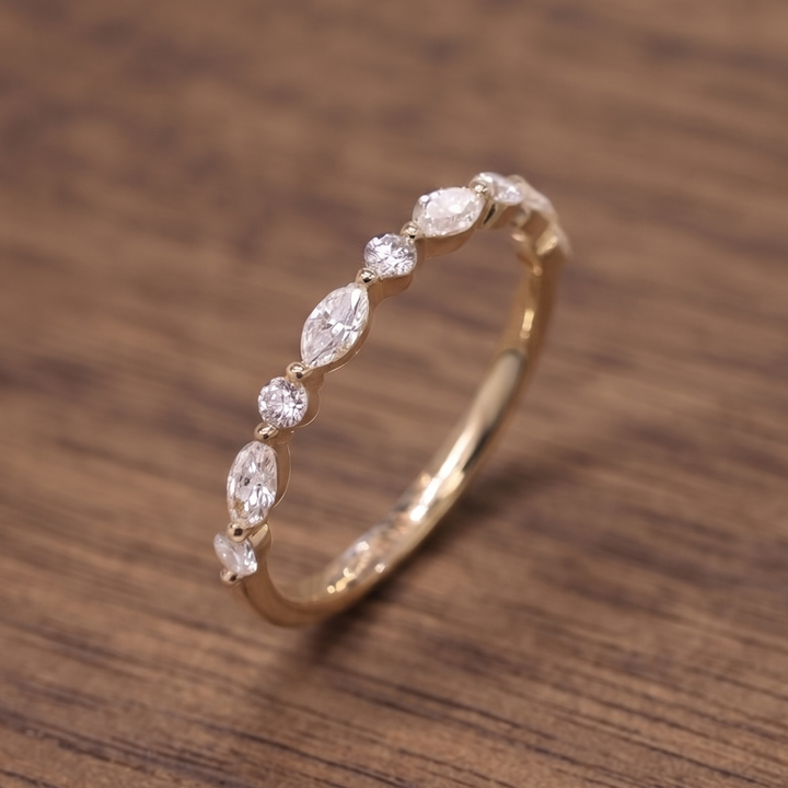 A gold ring featuring a row of marquise and round-cut clear gemstones, displayed on a brown wooden surface.