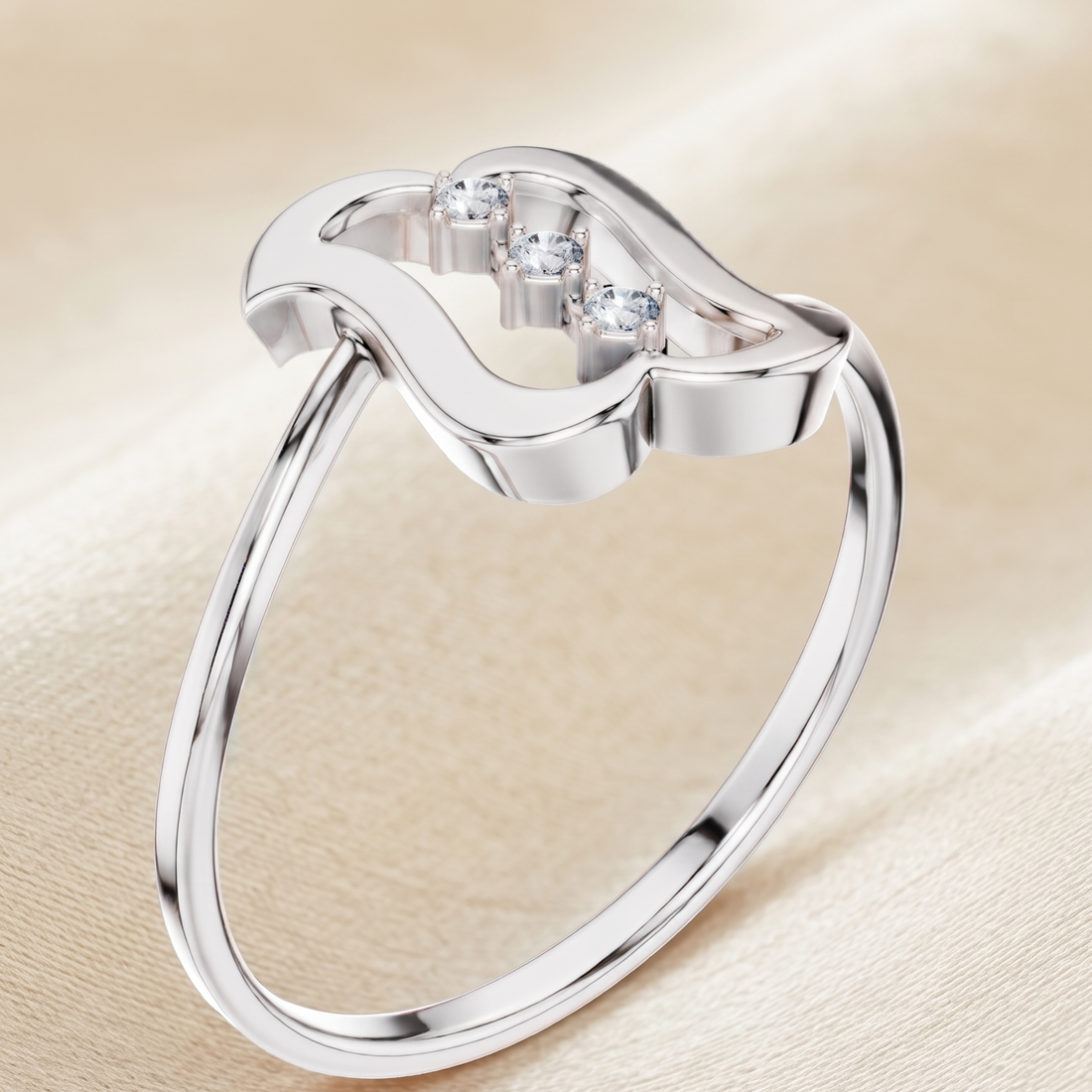 A polished silver ring with a wavy openwork top and three small clear gemstones, displayed on a soft beige fabric background.