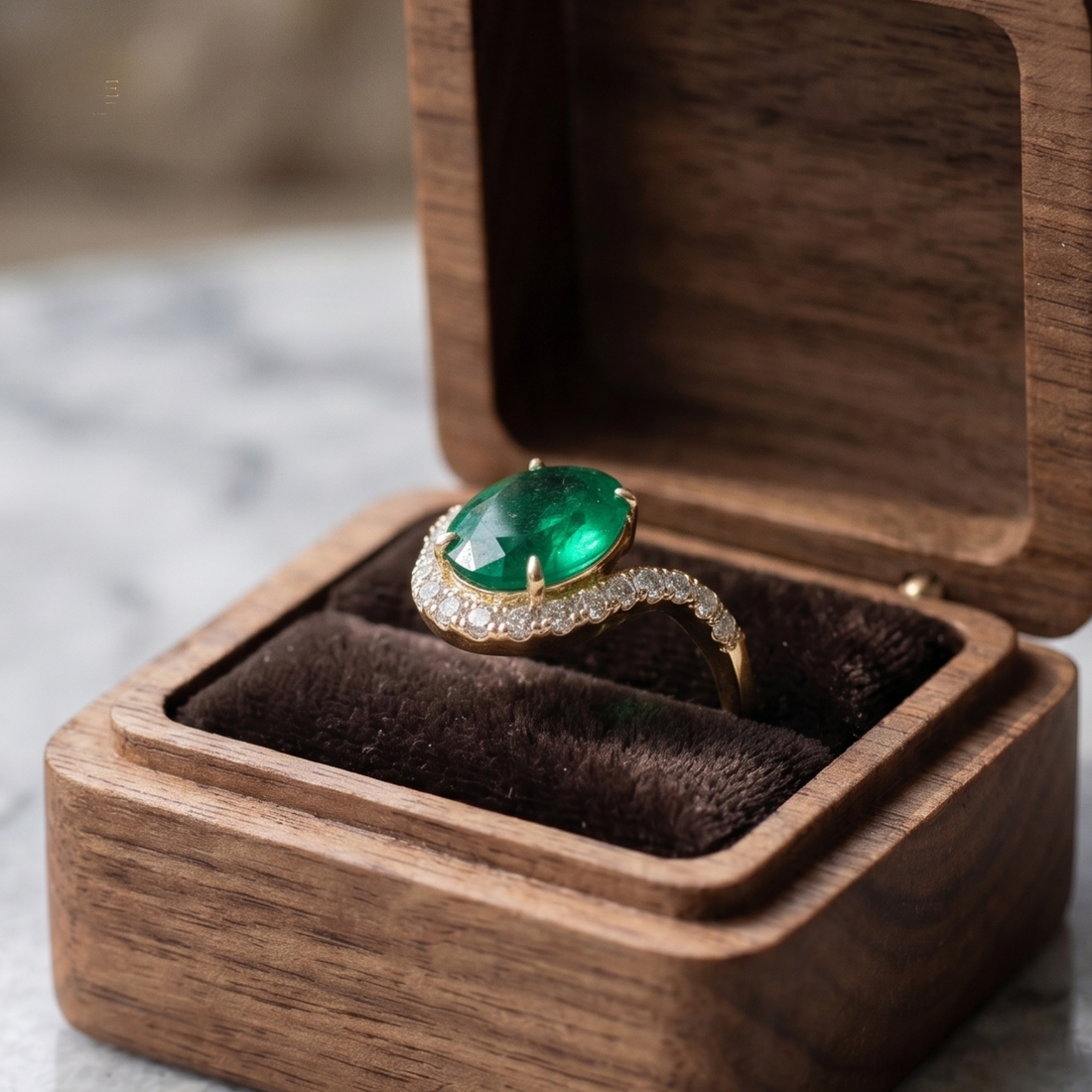 A gold ring with a large oval green emerald-cut center stone and a curved pavé band, displayed inside an open wooden jewelry box with a dark velvet lining.