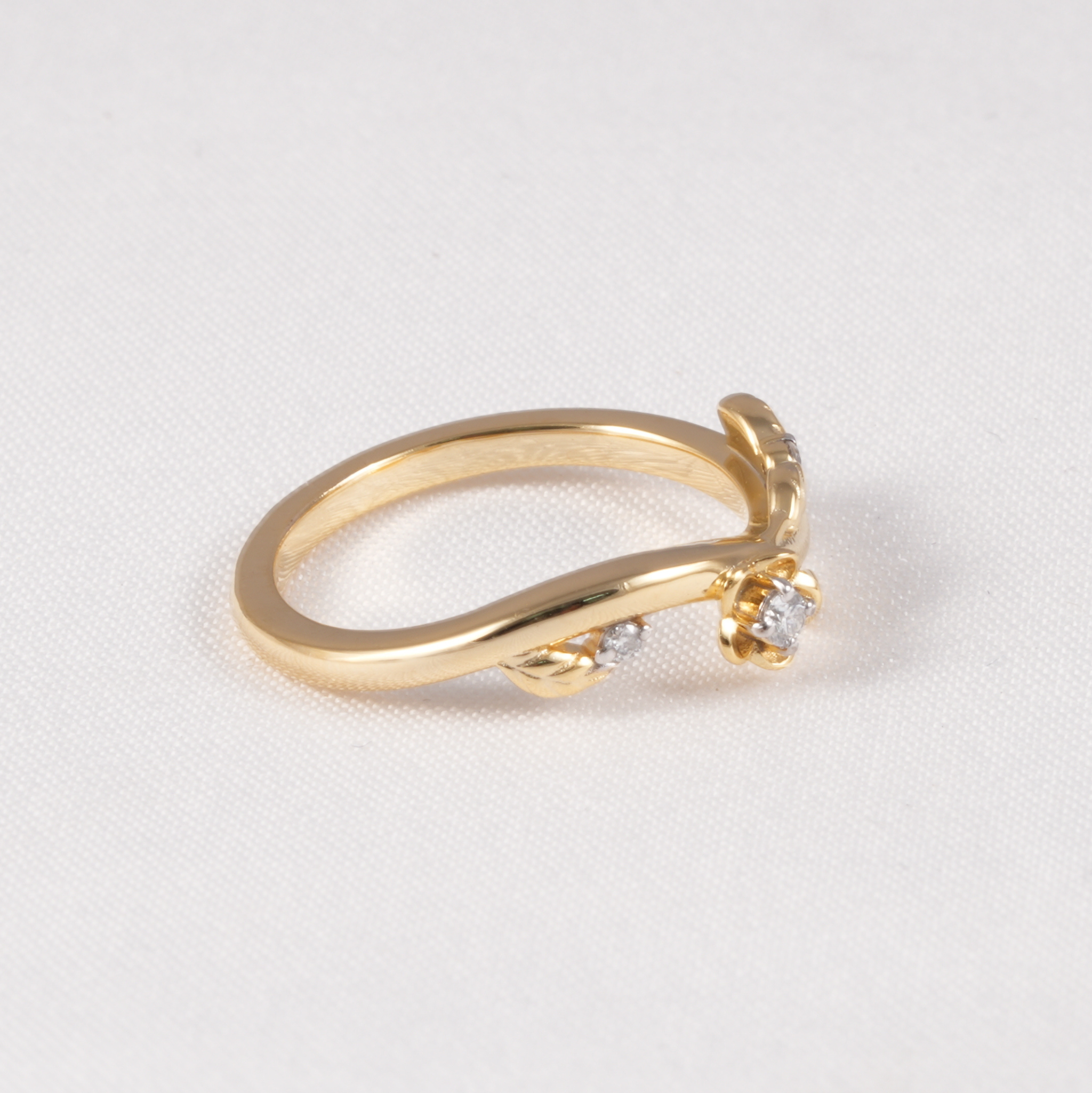 A yellow gold ring with a curved band and a small flower-shaped cluster of clear gemstones on the front, photographed on a light textured background.