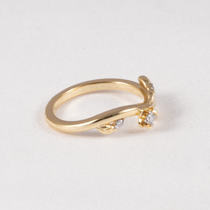 A yellow gold ring with a curved band and a small flower-shaped cluster of clear gemstones on the front, photographed on a light textured background.