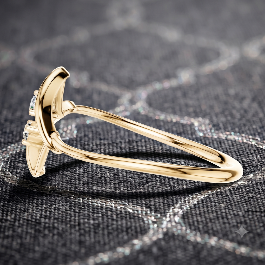 A close-up of a gold ring with a curved, sculptural setting and small clear stones, resting on a dark textured fabric background.