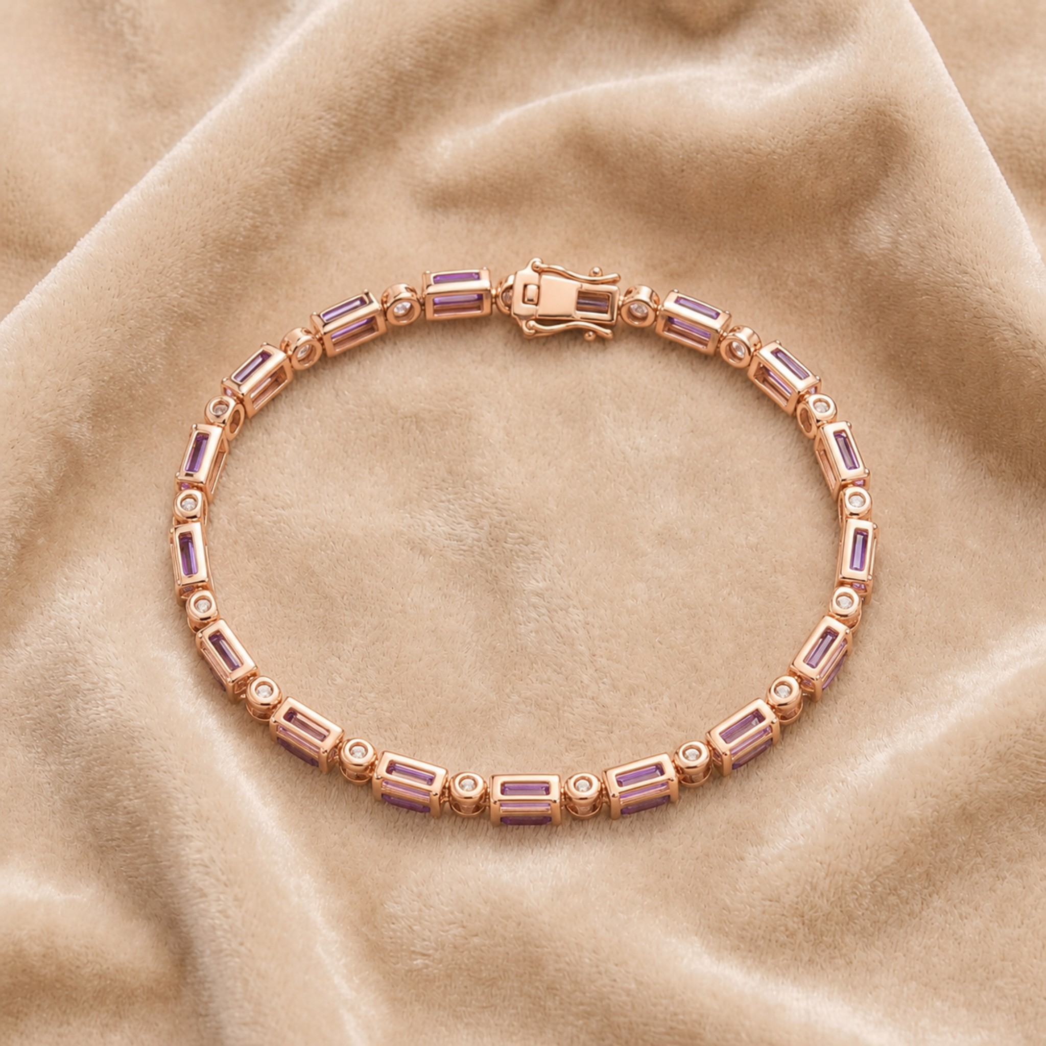 A rose gold tennis bracelet with rectangular purple crystals and small clear stones, displayed on a beige velvet fabric background.
