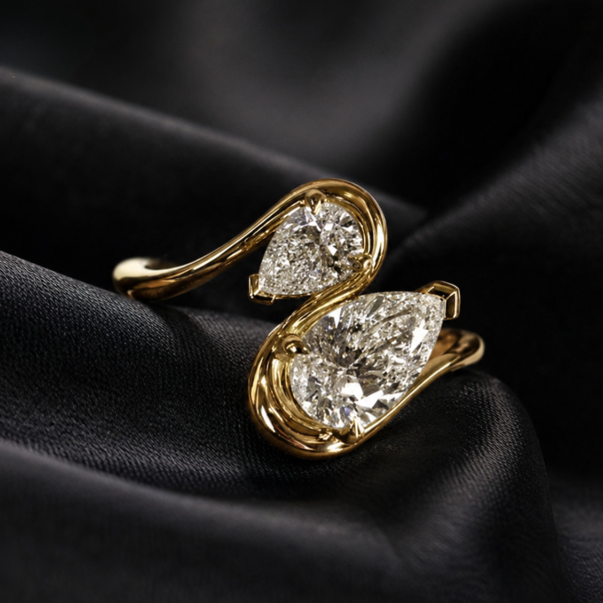 A gold ring with two pear-cut clear gemstones, displayed on draped black satin fabric.