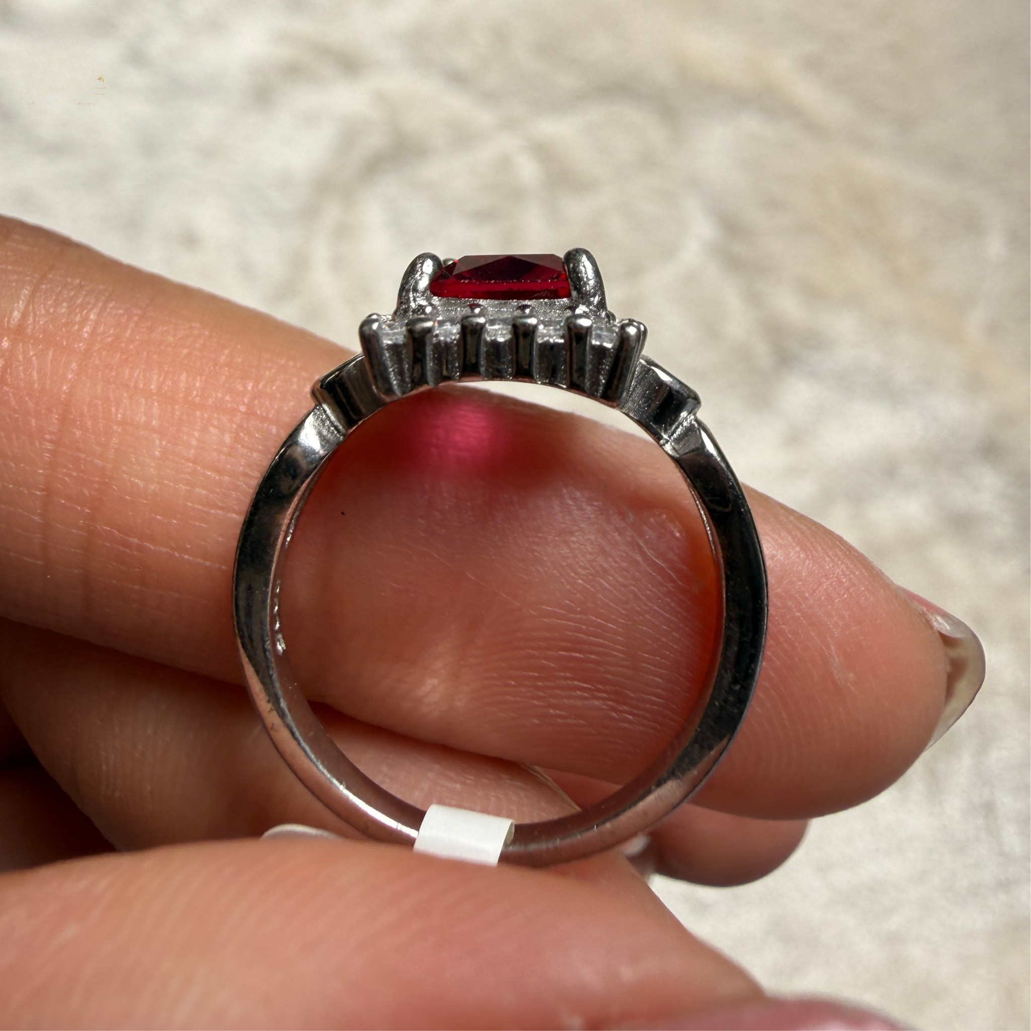 A sterling silver ring with a rectangular red gemstone and small clear accent stones, held between fingers against a light textured background.