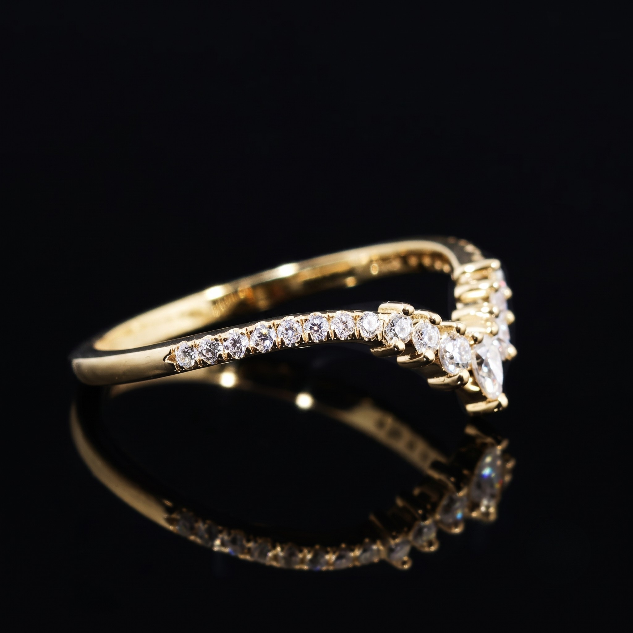 A gold ring with a curved row of clear stones, photographed on a glossy black reflective surface.
