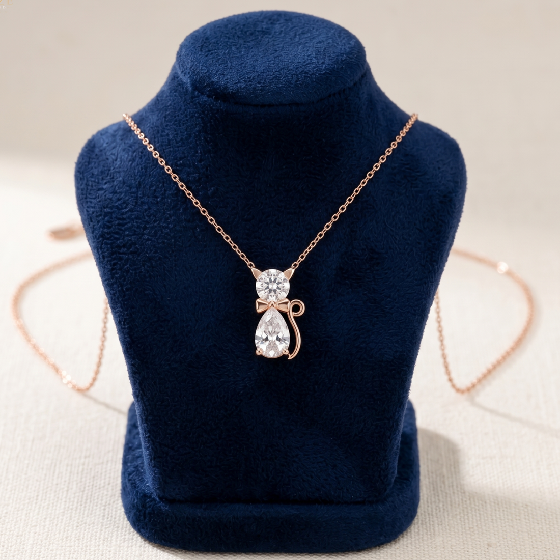 Rose gold necklace with a teardrop-shaped clear crystal pendant and a small bow detail, displayed on a dark blue velvet jewelry bust.