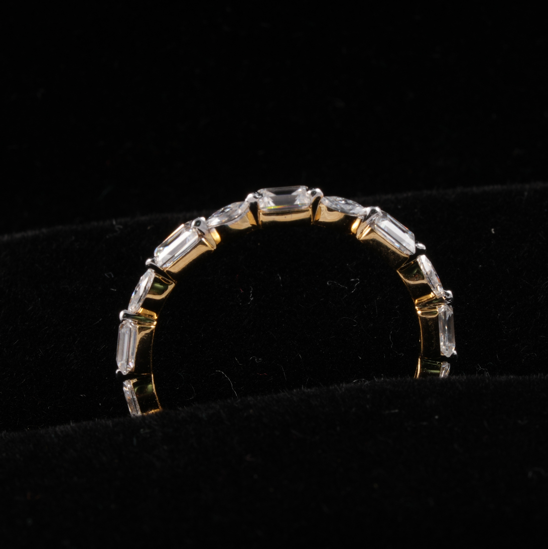A gold ring featuring a row of baguette-cut clear gemstones, displayed on a black velvet jewelry stand.