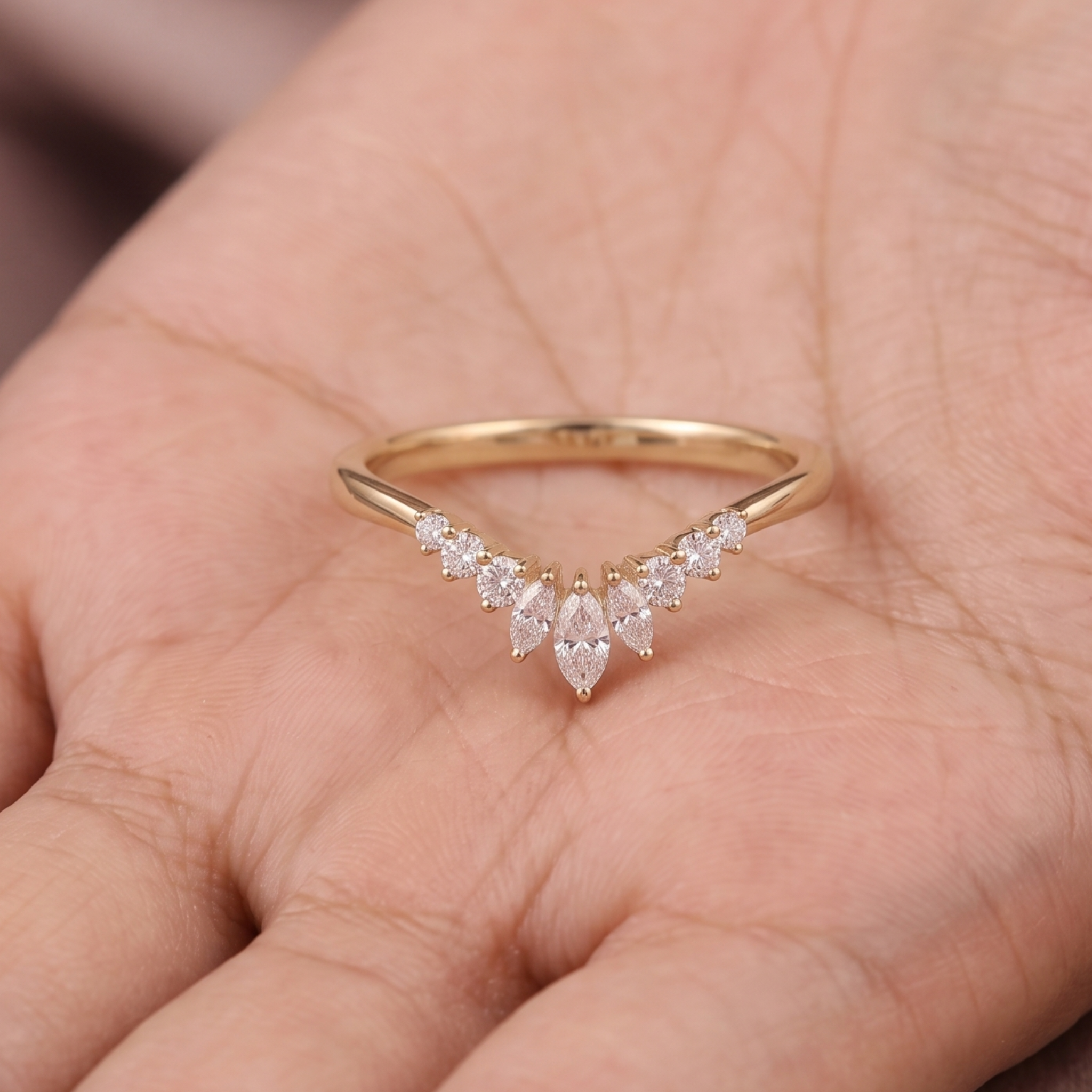 A gold V-shaped ring with marquise-cut clear gemstones, resting on a person's palm.
